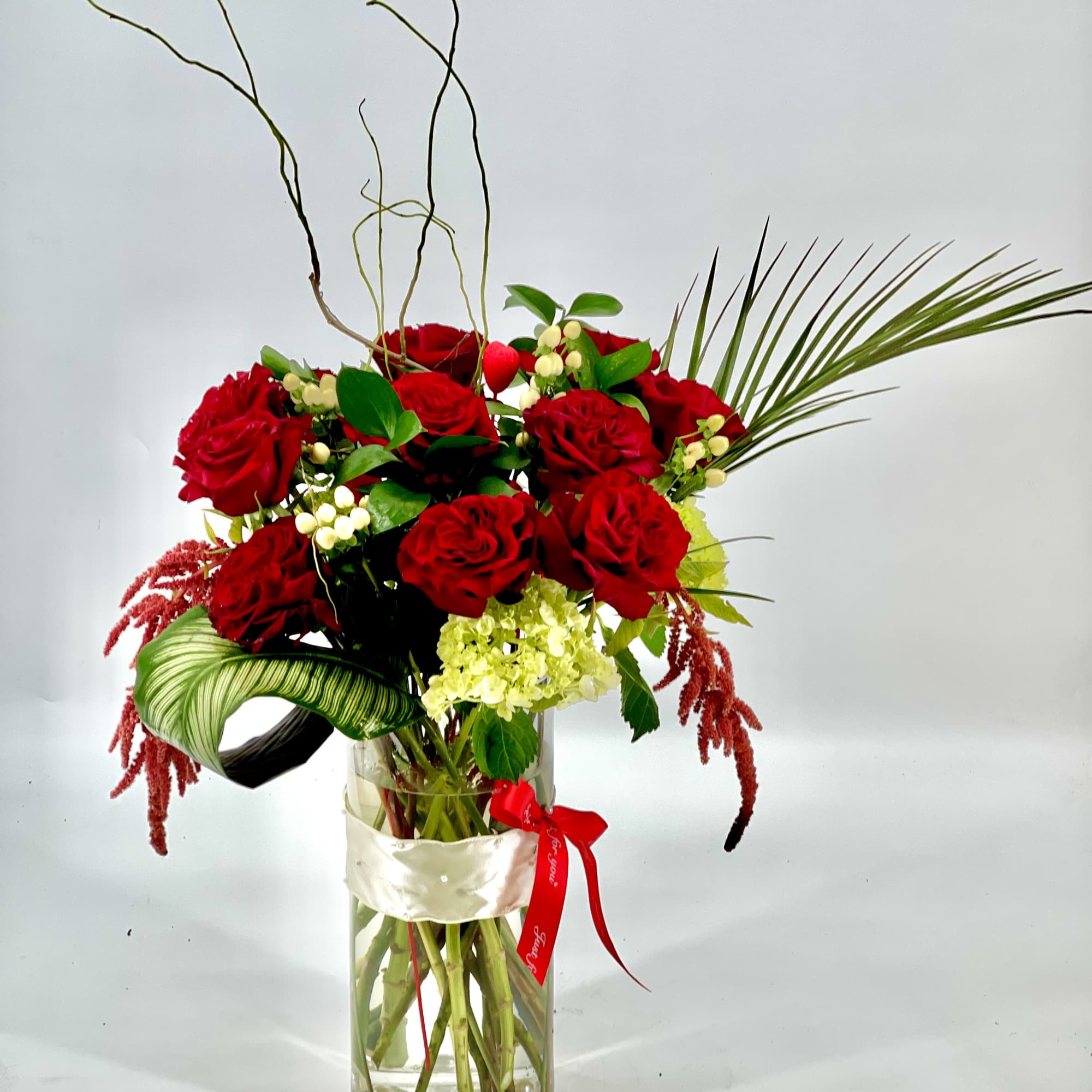 Red roses arranged in a tall glass vase with decorative branches and ribbon