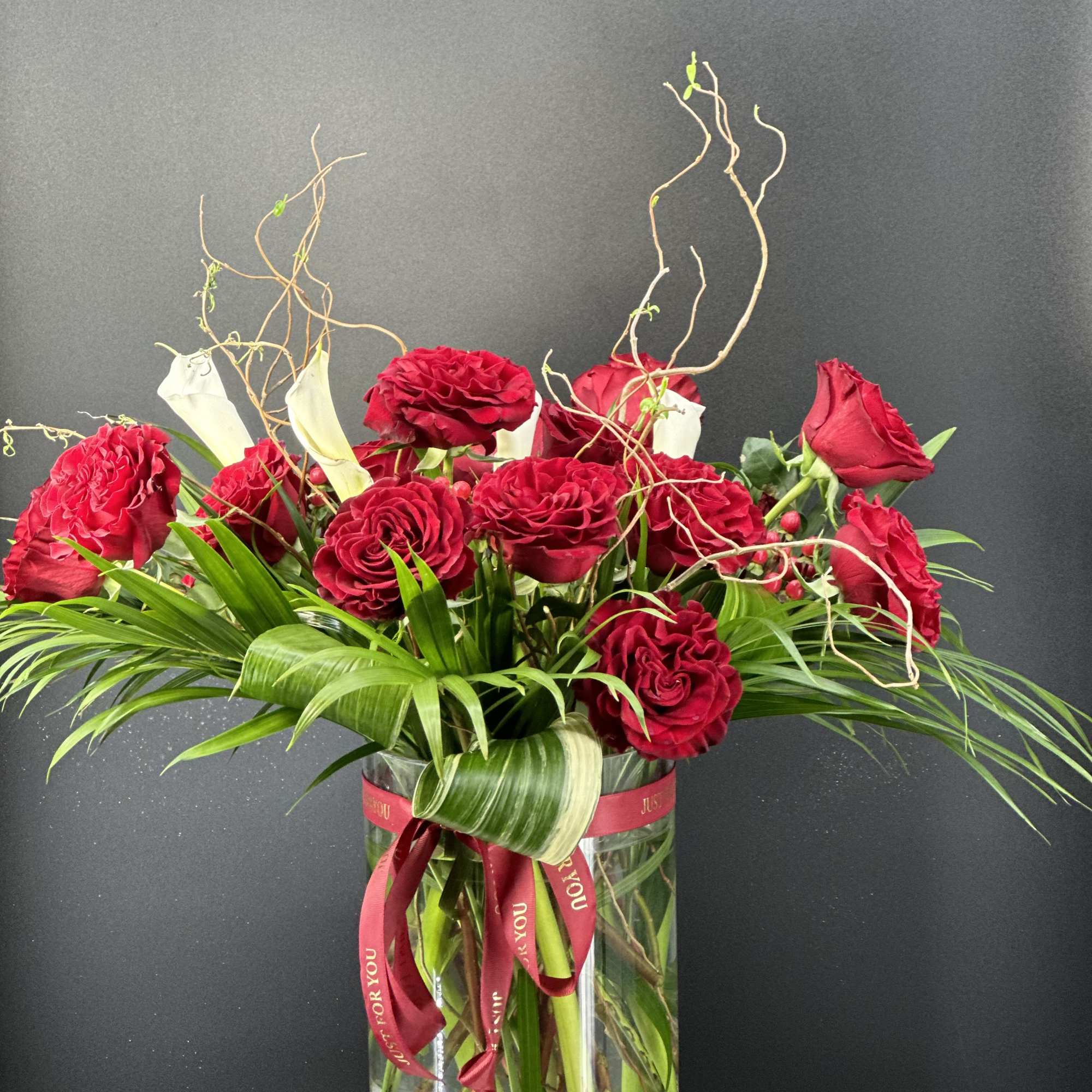 Red roses and white calla lilies in a clear glass vase with a ribbon