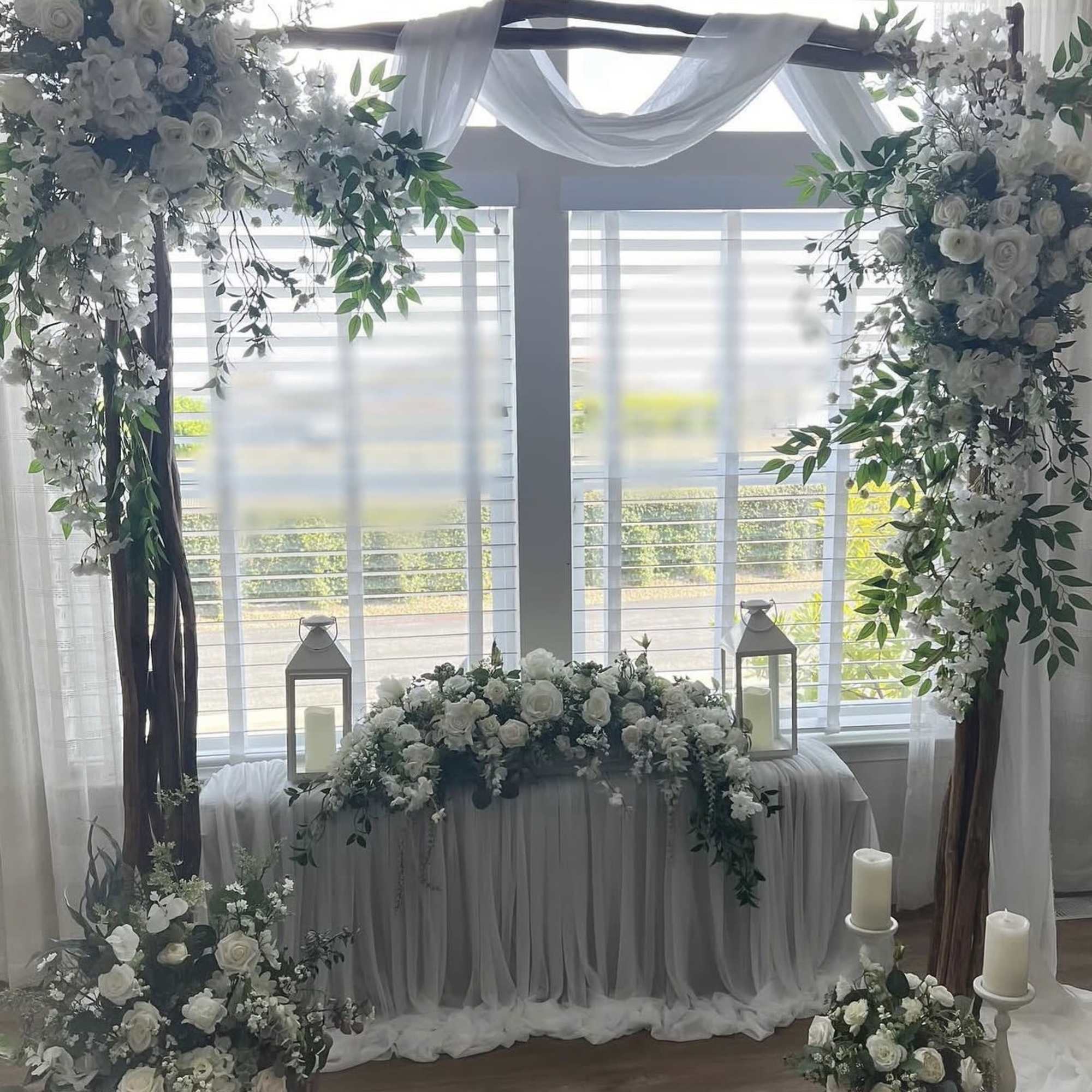 A soft, romantic wedding arrangement built around a white-draped wooden arch that