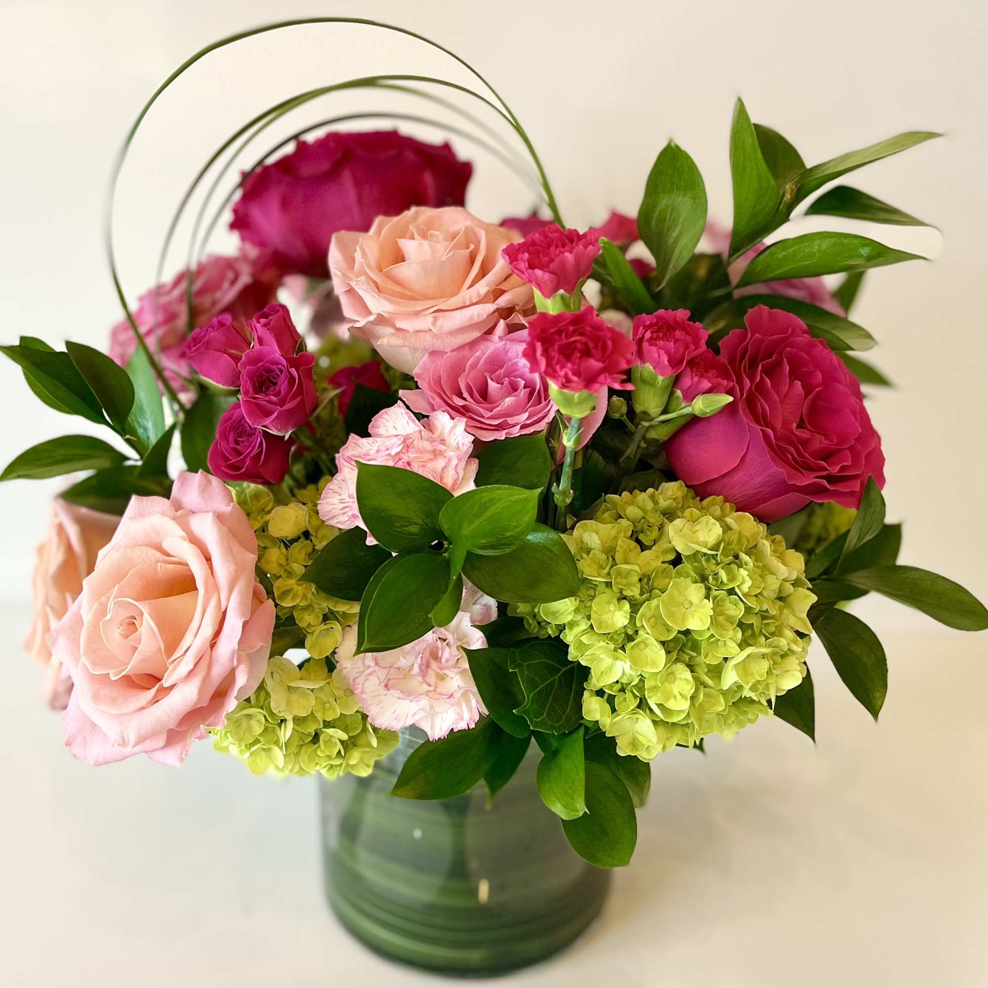 Pink and peach roses with green hydrangeas in a glass vase