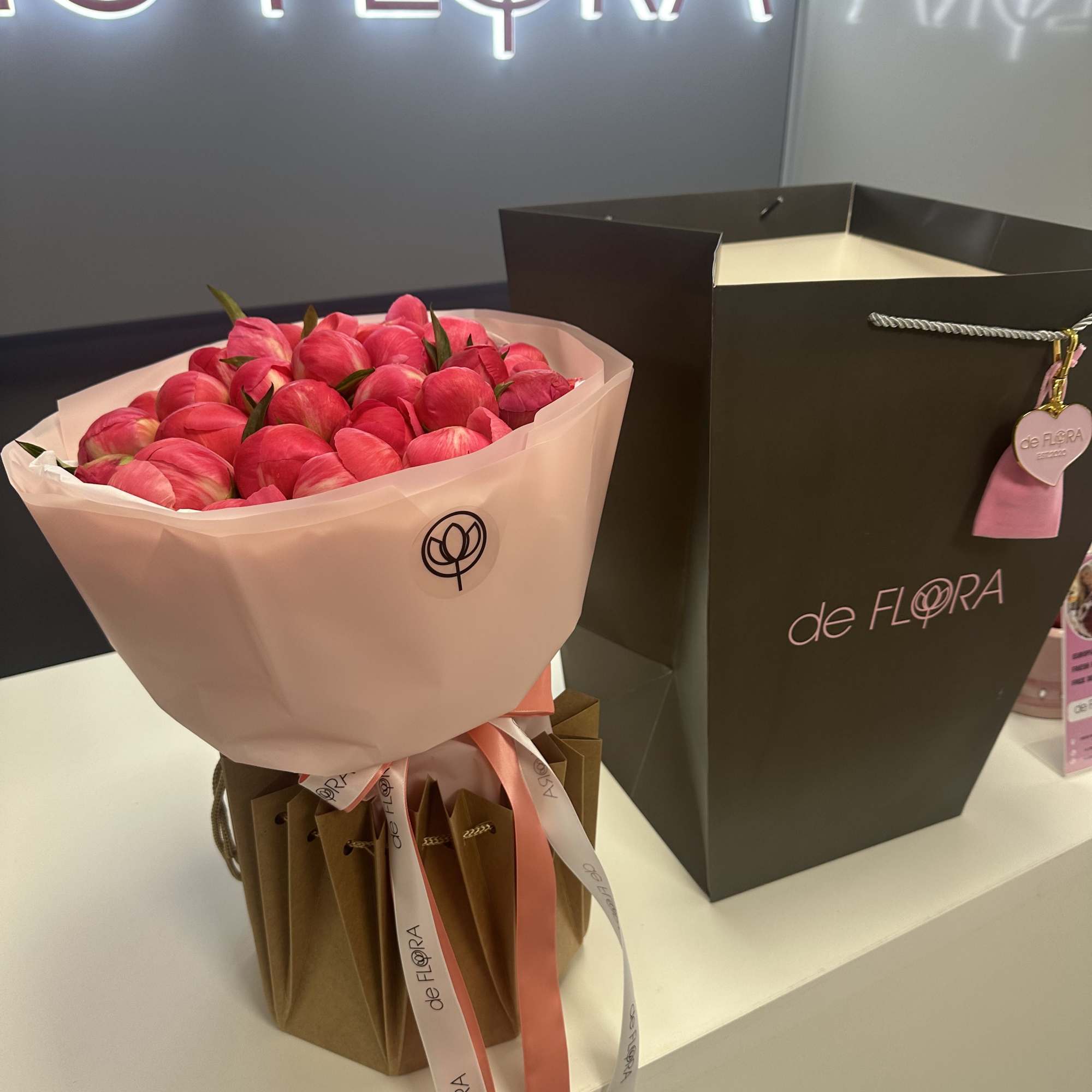 Bouquet of pink tulips wrapped in pale paper beside a black gift bag