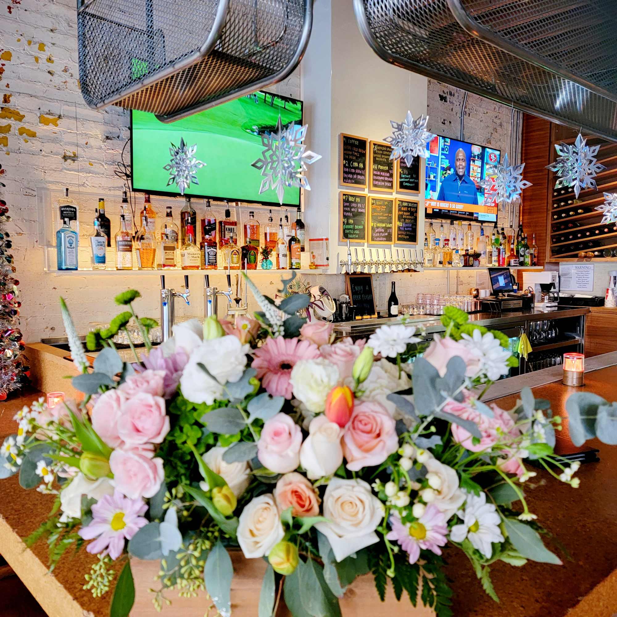 Pastel pink and white roses, daisies, and tulips arranged in a wooden box centerpiece on a bar counter