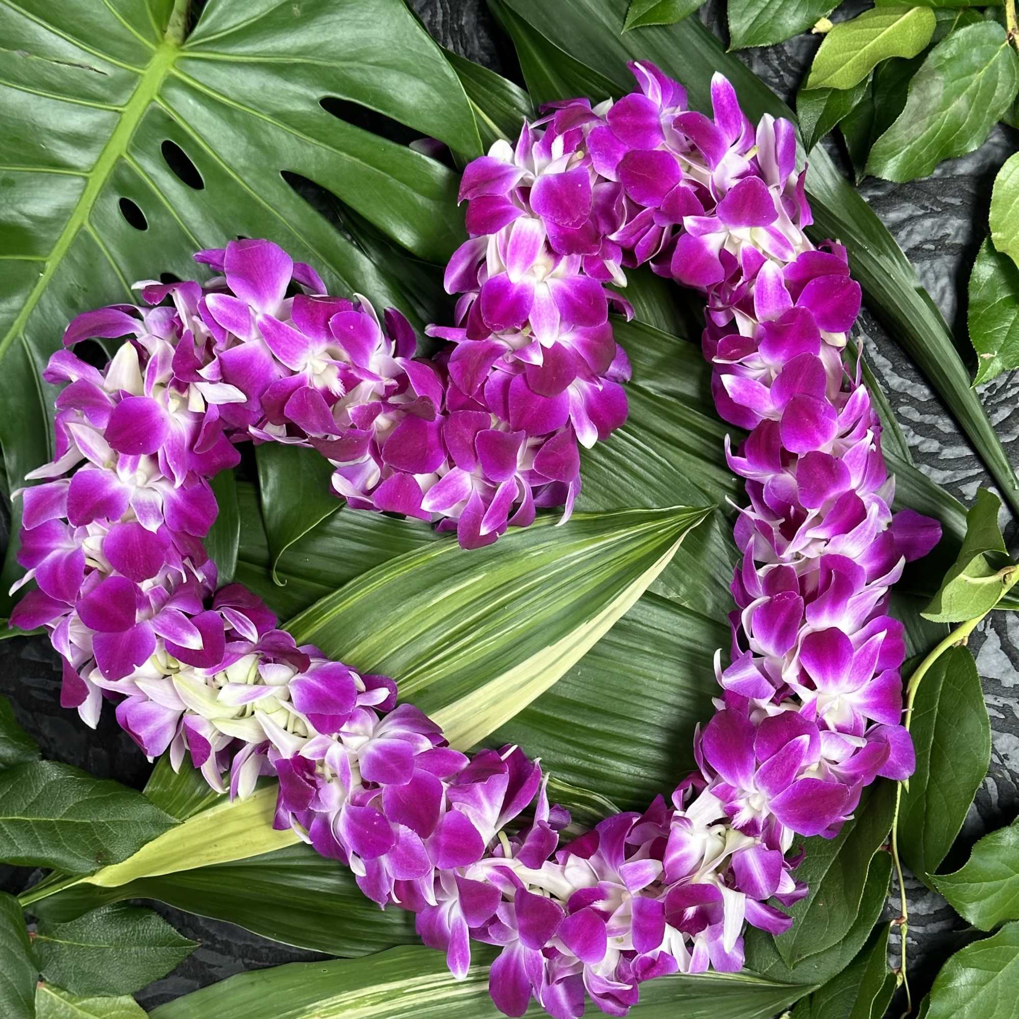 Purple orchid lei on a bed of tropical leaves