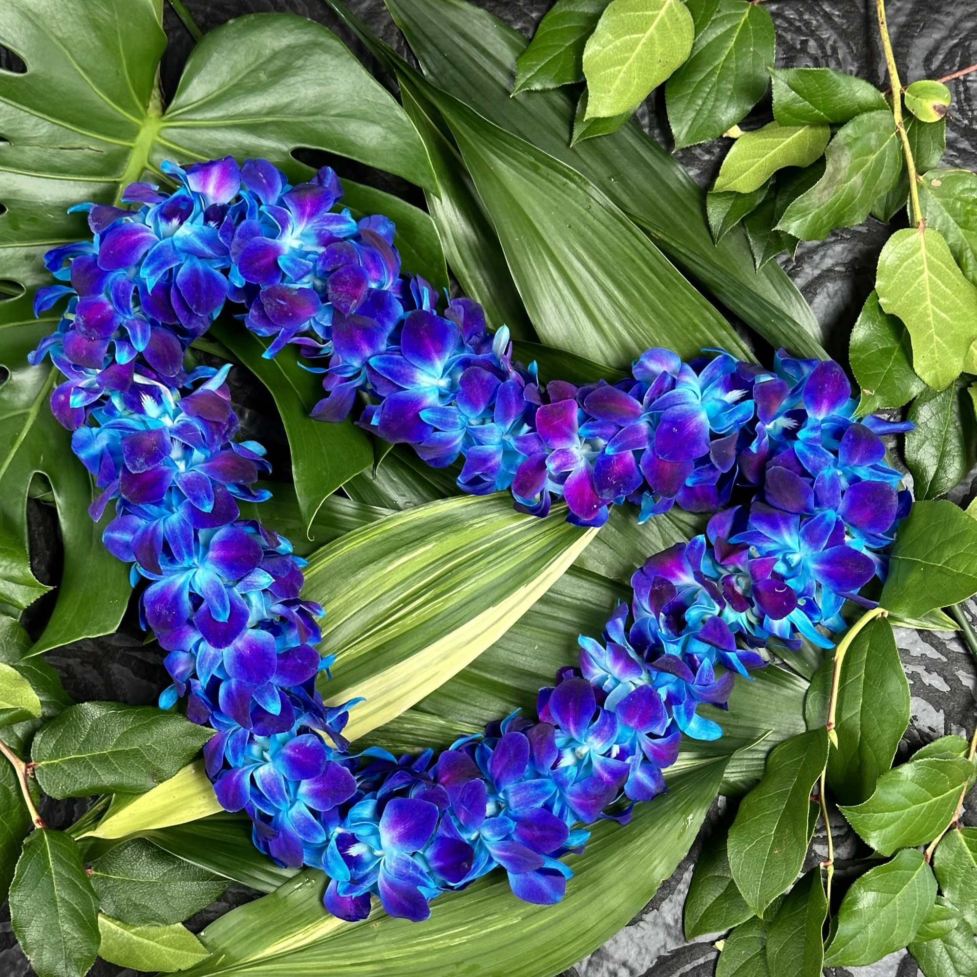 Blue and purple flower lei on a bed of green leaves