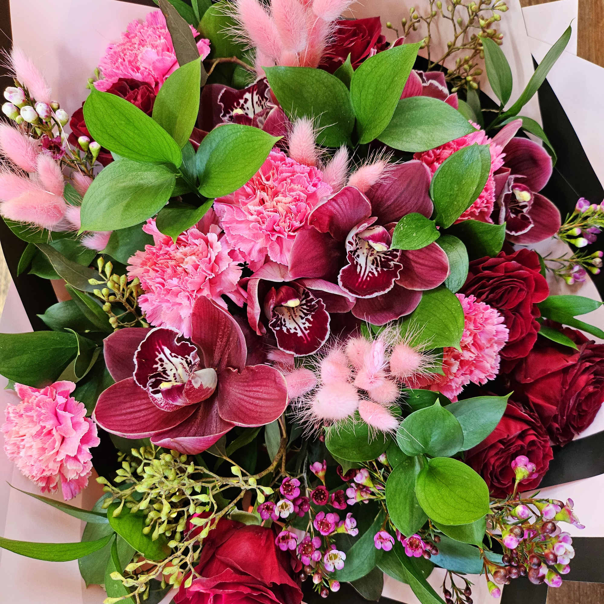 Bouquet of pink and burgundy flowers with green leaves and black-and-white wrapping