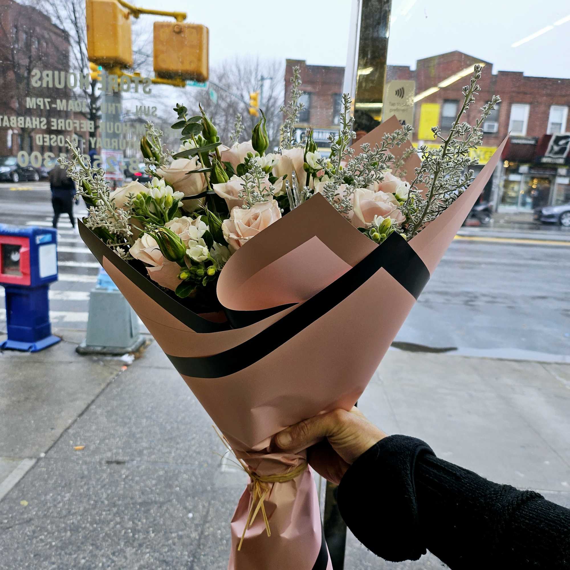 Handheld bouquet of pale pink roses and white blooms wrapped in pink paper