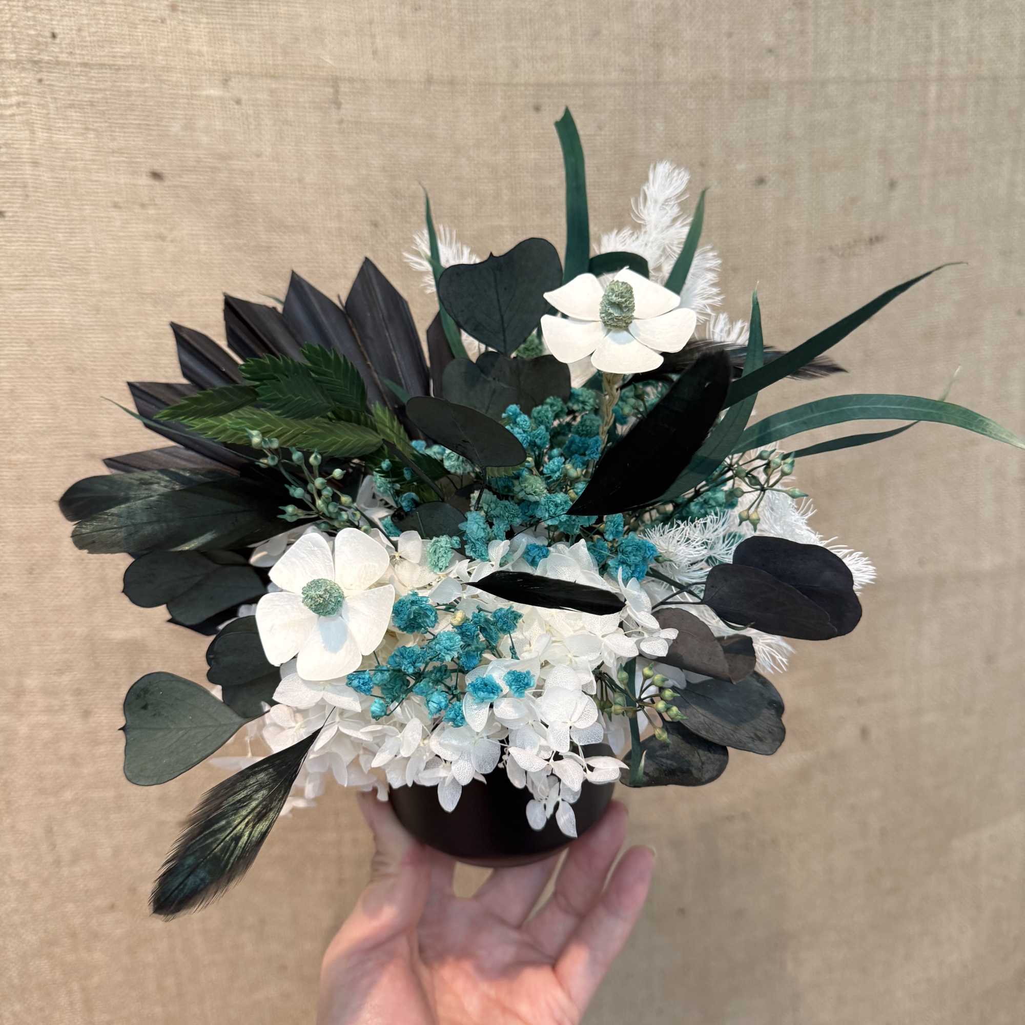 Small black-and-white floral arrangement with blue accents in a dark vase
