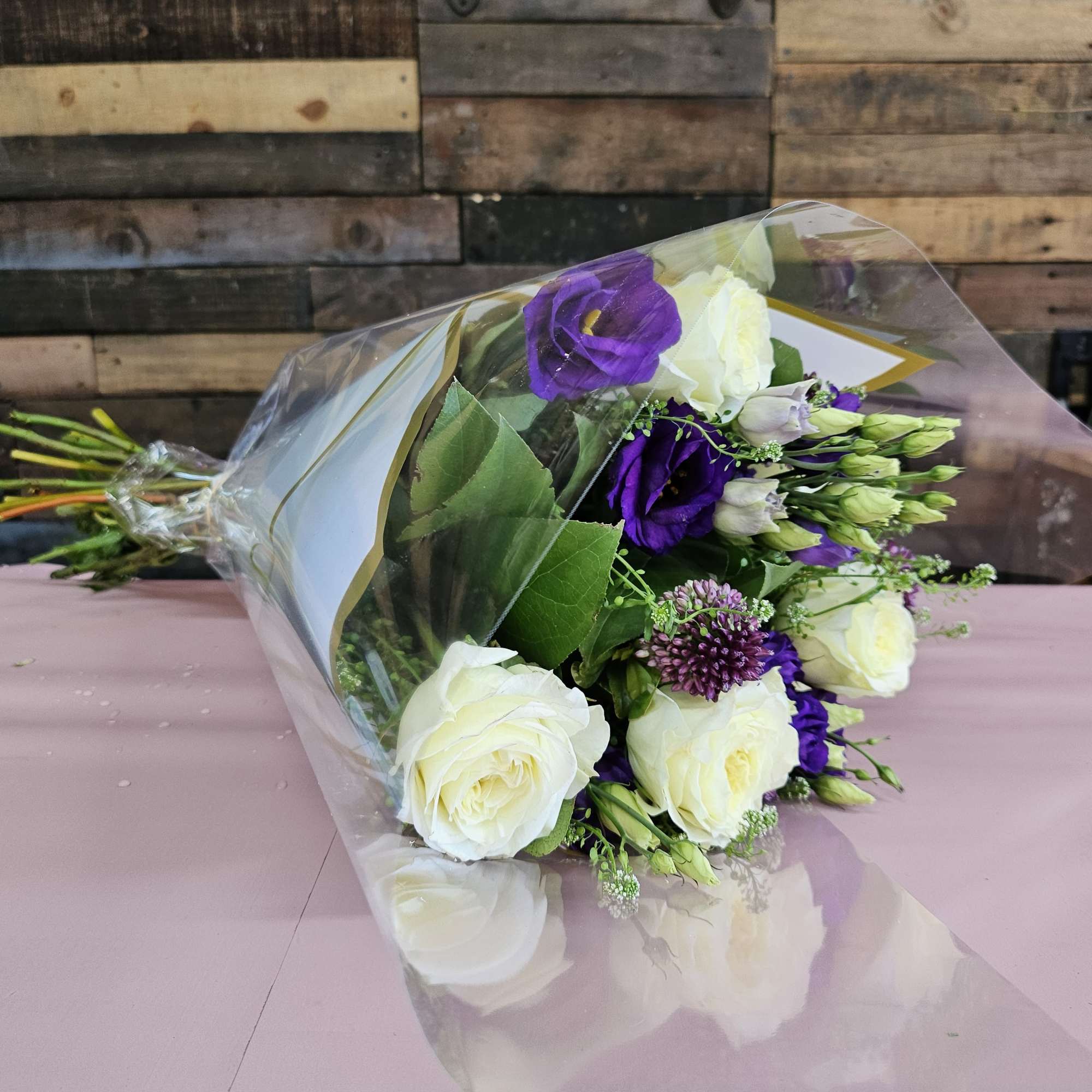 Bouquet of white roses and purple lisianthus wrapped in clear plastic