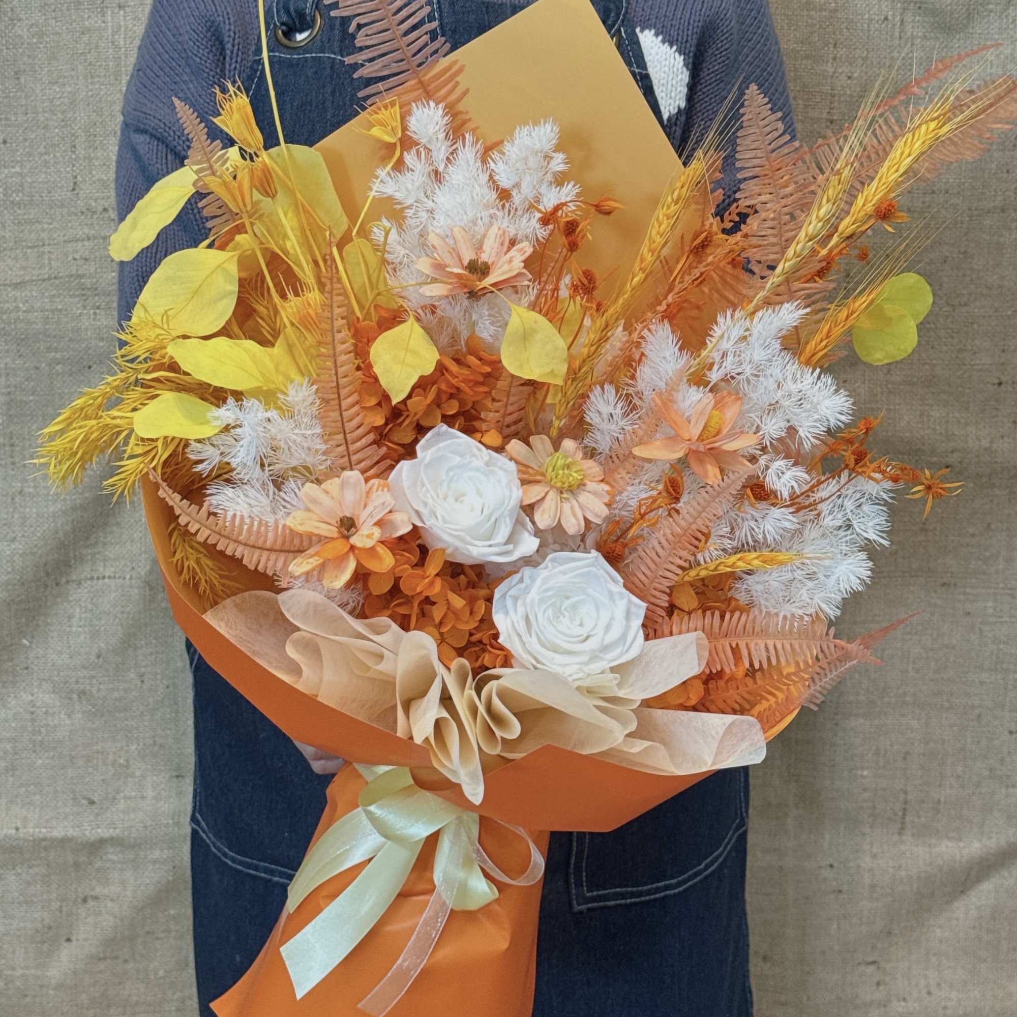 Tall bouquet of orange, yellow, and white flowers wrapped in bright orange paper with a pale ribbon