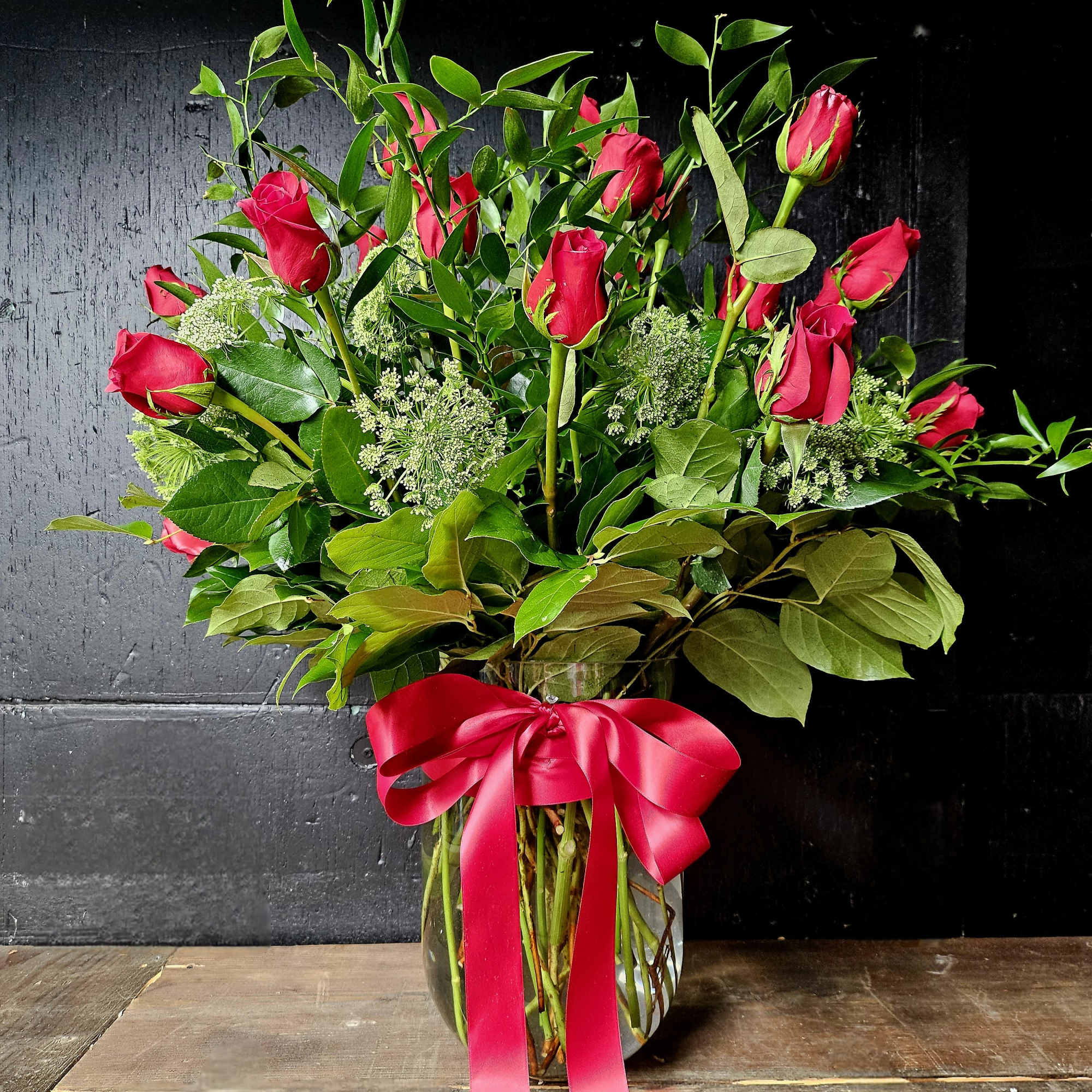 Red roses in a clear glass vase with a pink ribbon