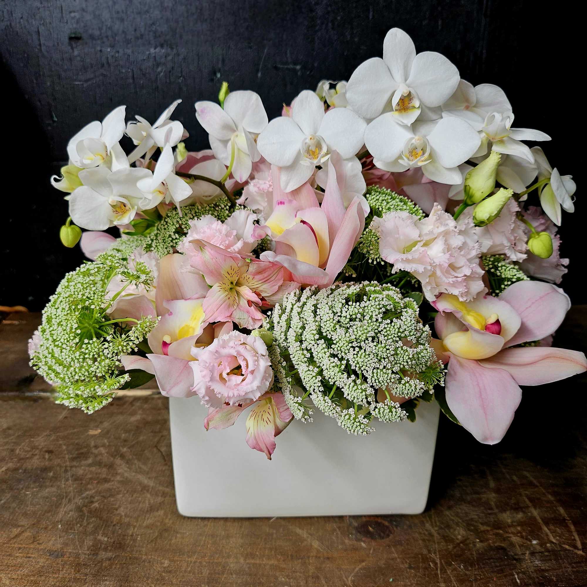 Pink and white orchid arrangement in a white square vase