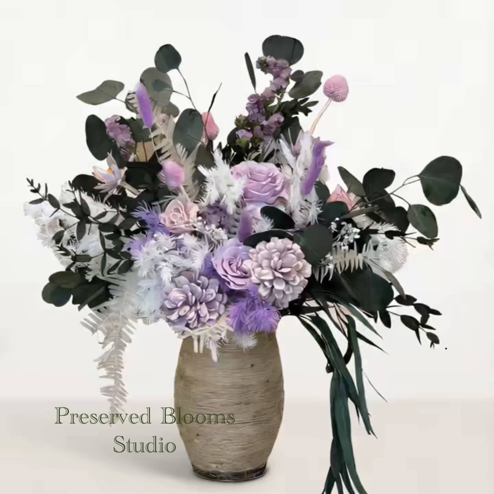 Tall arrangement of lavender and white preserved flowers with dark greenery in a textured beige vase