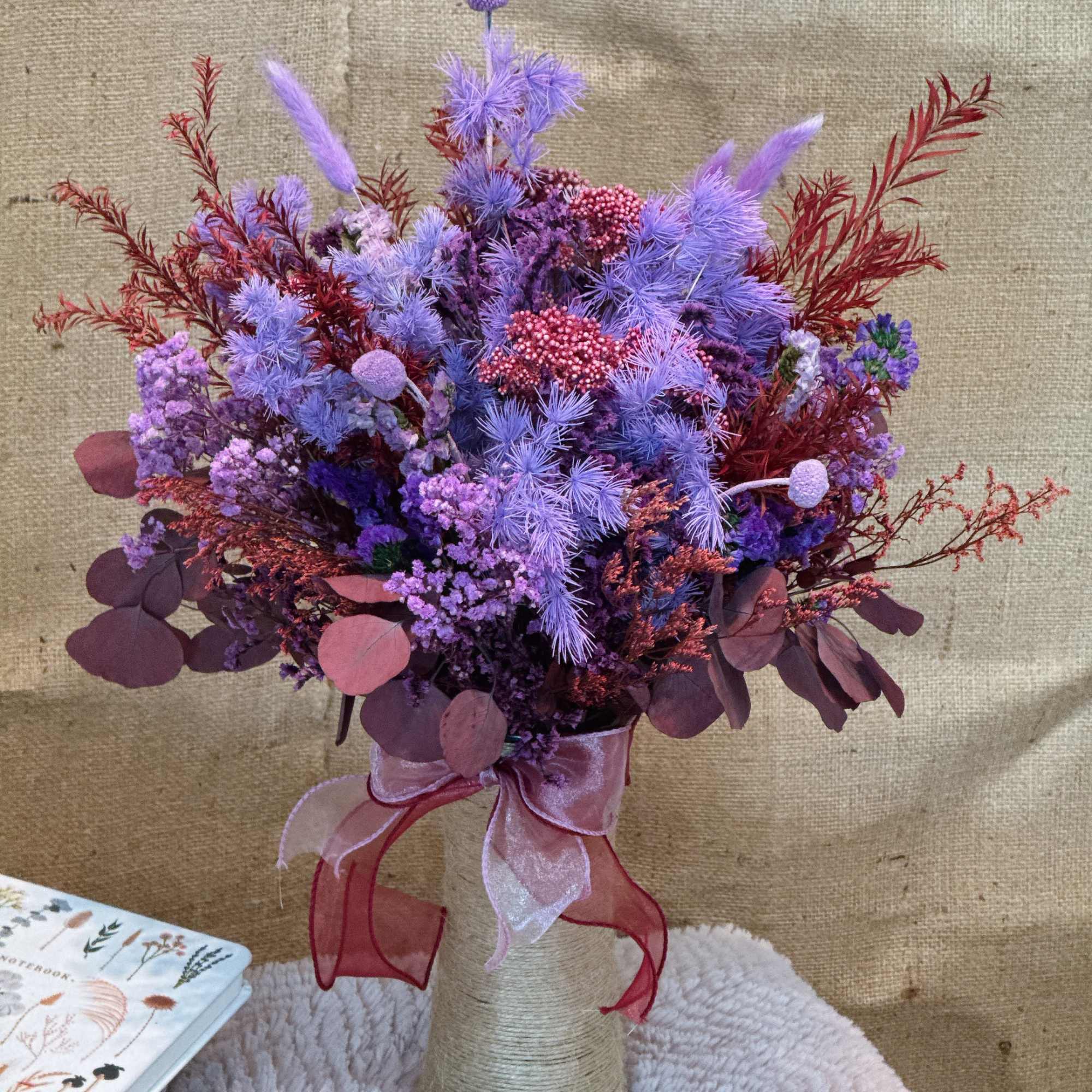 Lavender and burgundy bouquet in a twine-wrapped vase with a pink ribbon bow.