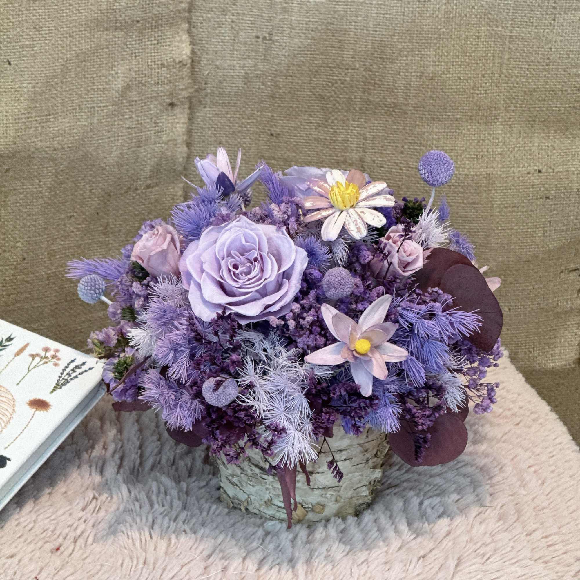 Low lavender and purple mixed flower arrangement in a rustic birch pot