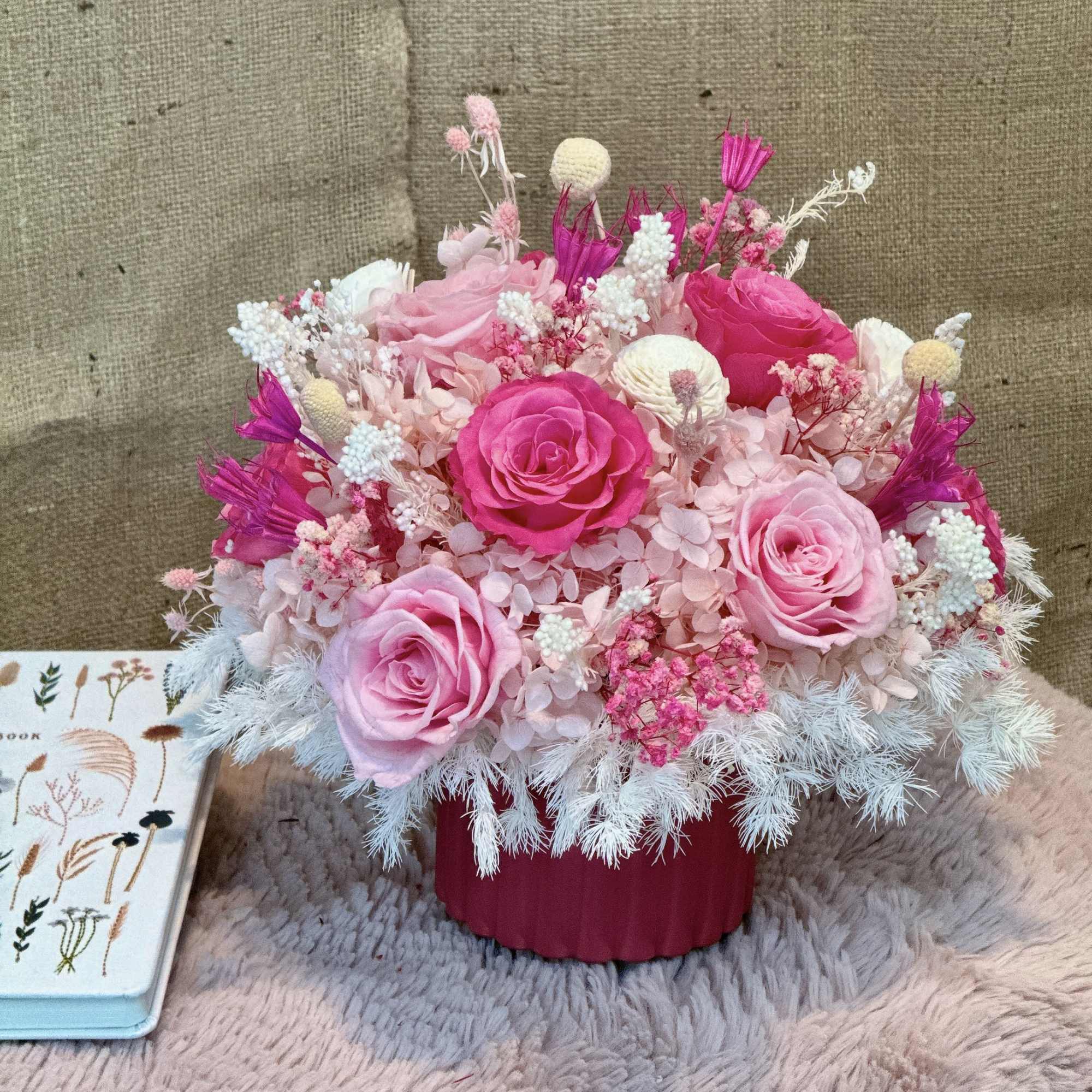 Compact arrangement of pink roses and mixed pink and white flowers in a pink pot
