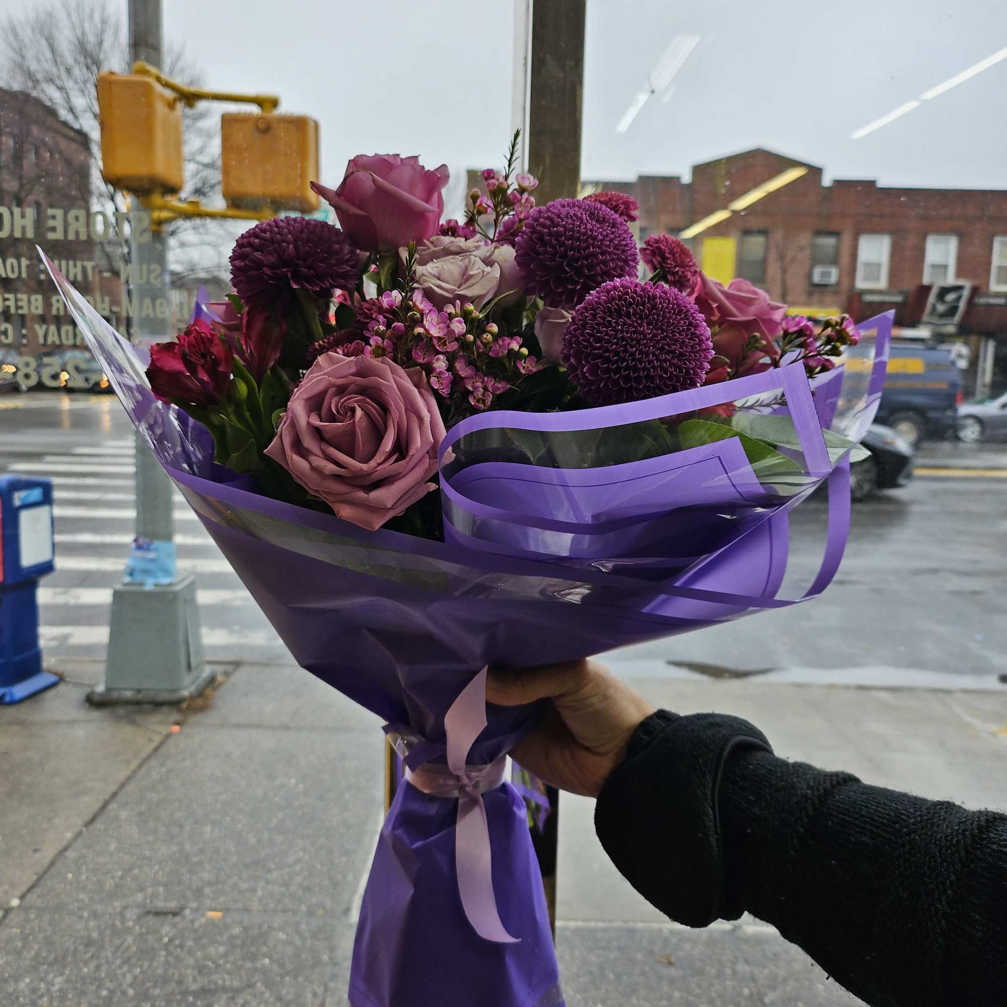 Purple bouquet of roses and round pompon flowers wrapped in purple paper