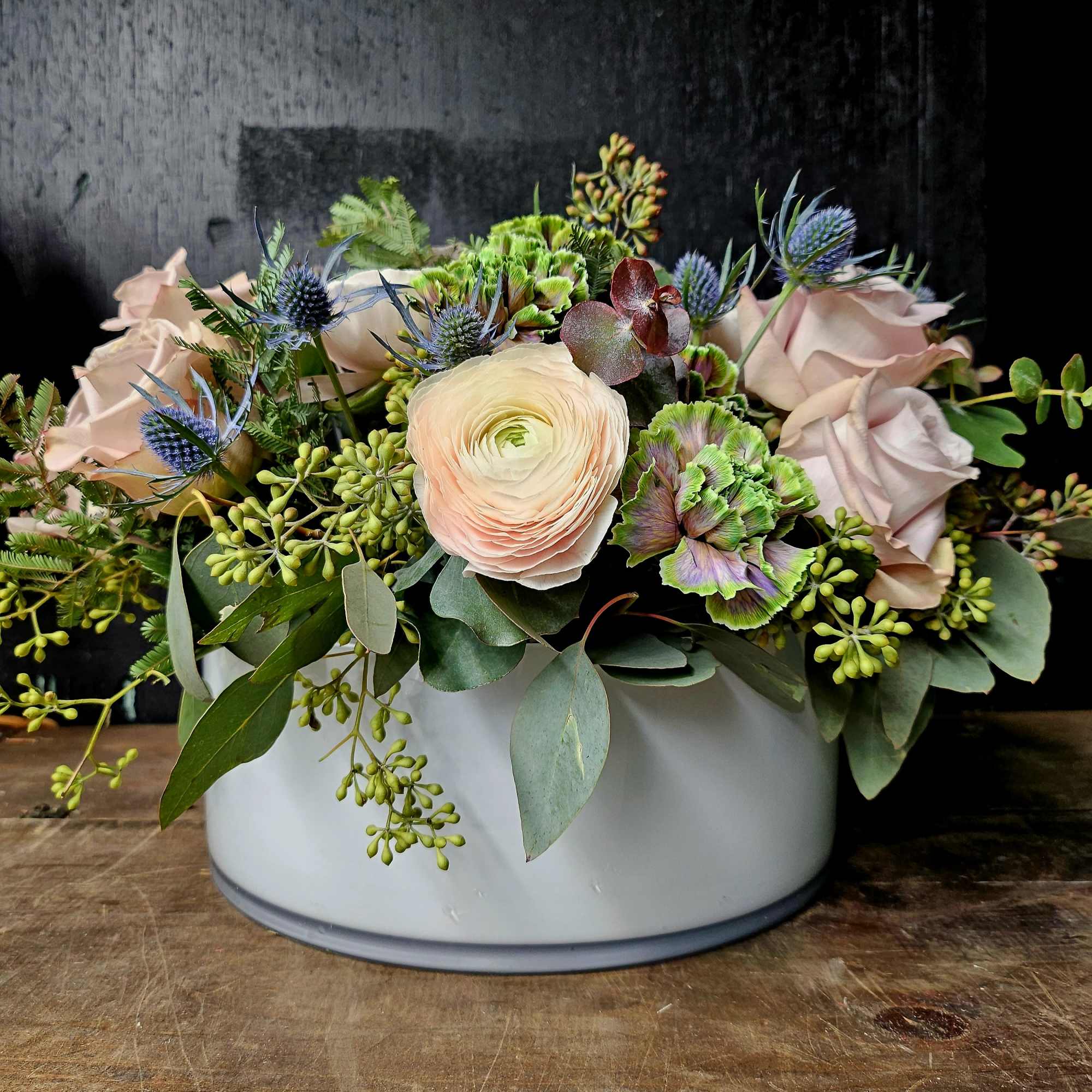 Mixed bouquet in a white round container with pale pink and green blooms