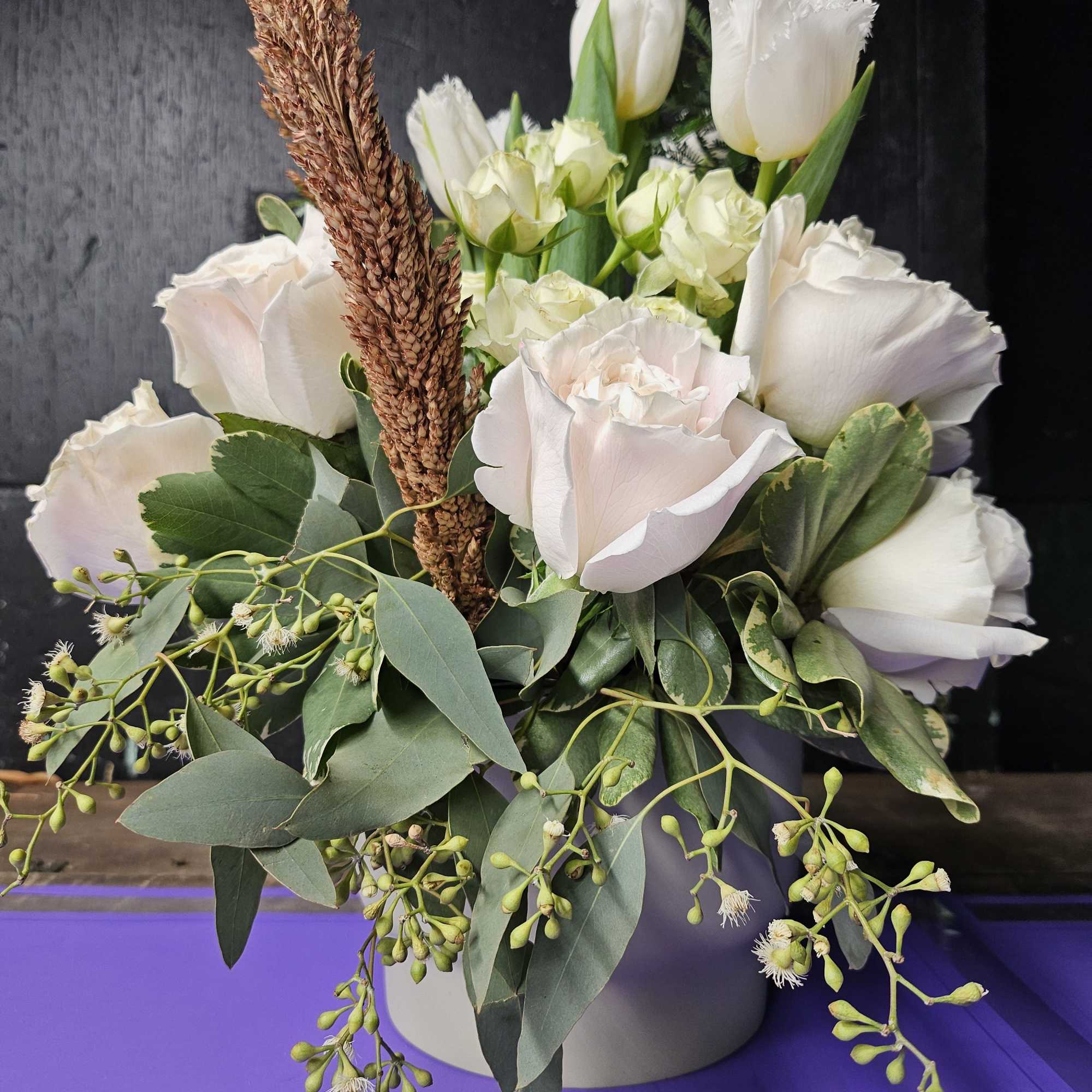 White roses and tulips arranged in a round vase with greenery