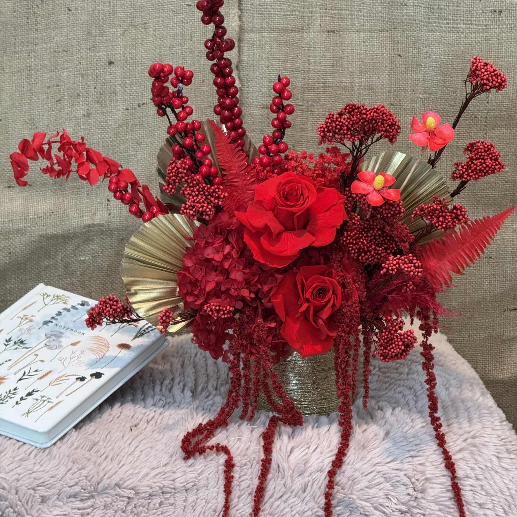 Red rose arrangement in a gold vase with berry-like accents
