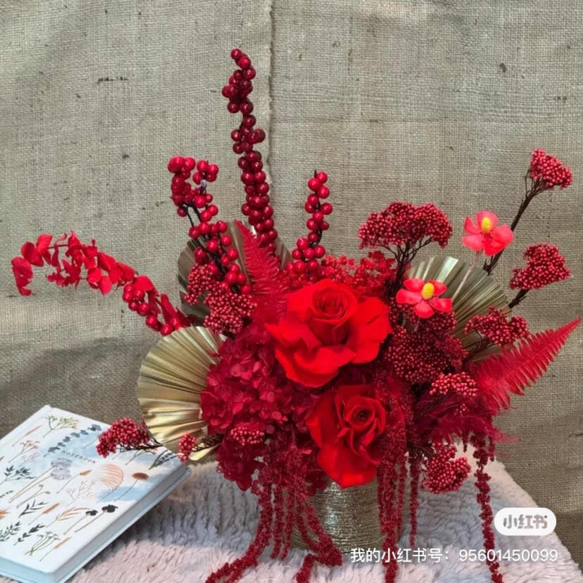 Red rose arrangement with berry-like accents and gold fan leaves