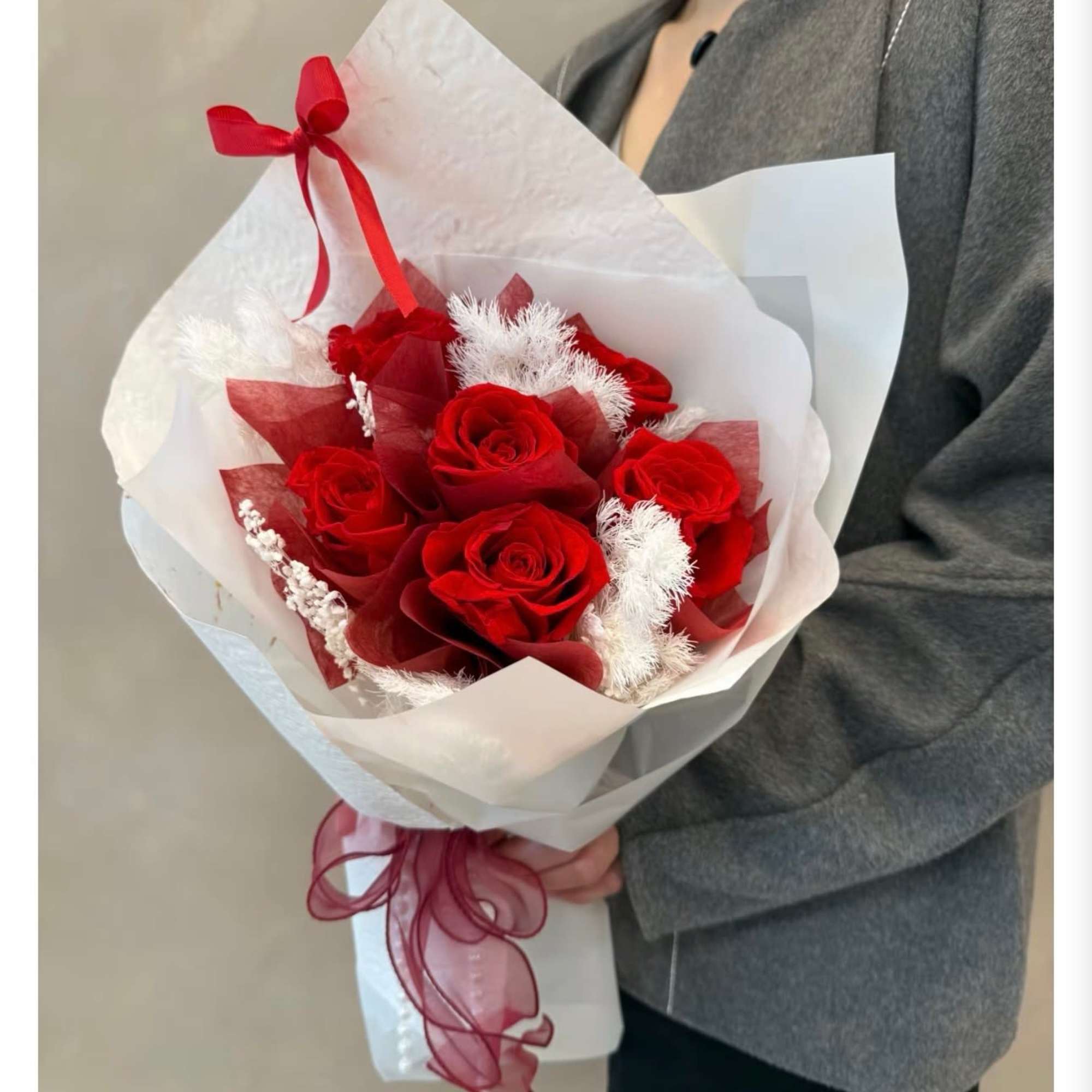 Bouquet of red roses wrapped in white paper with red ribbon