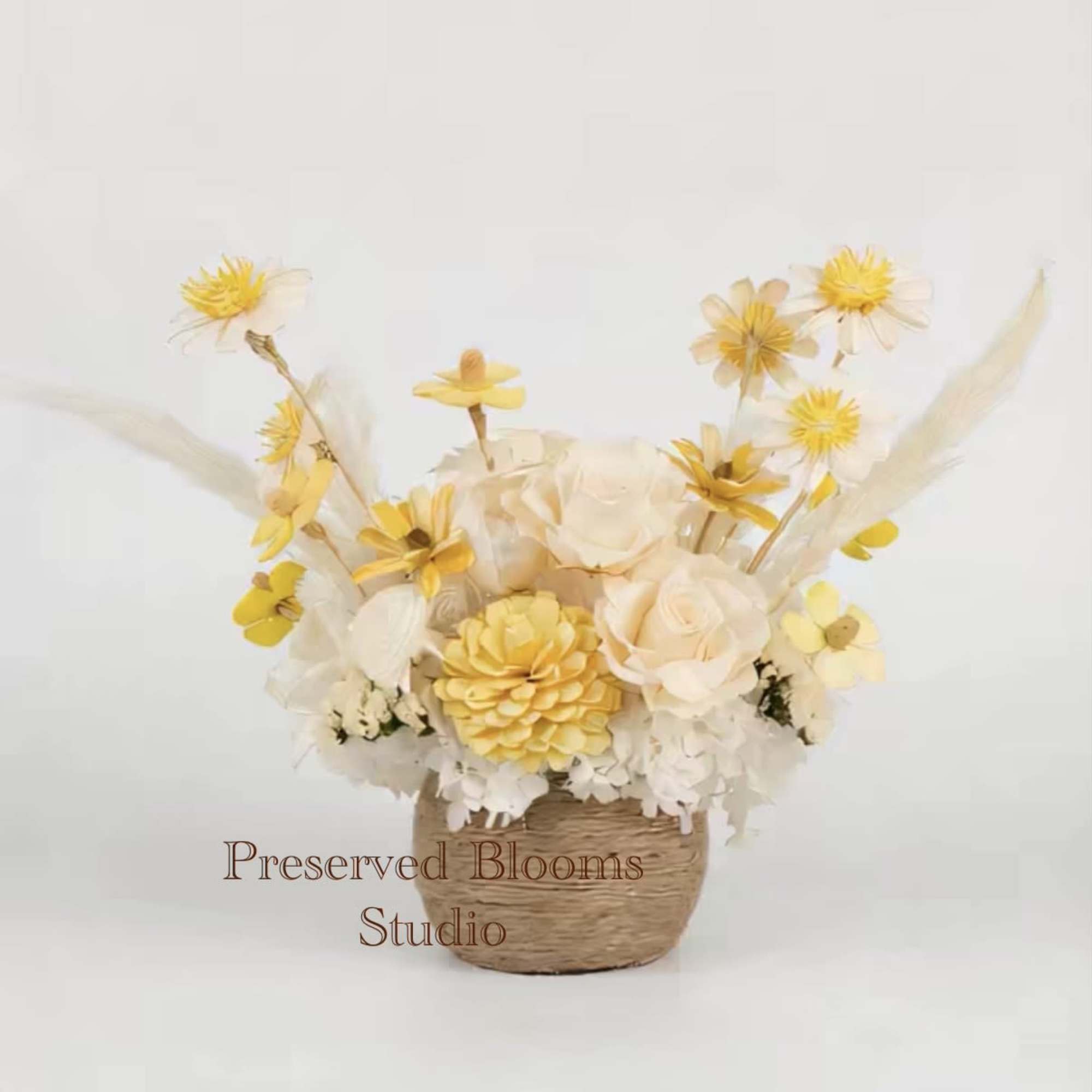 Yellow and cream preserved flower arrangement in a small woven basket container
