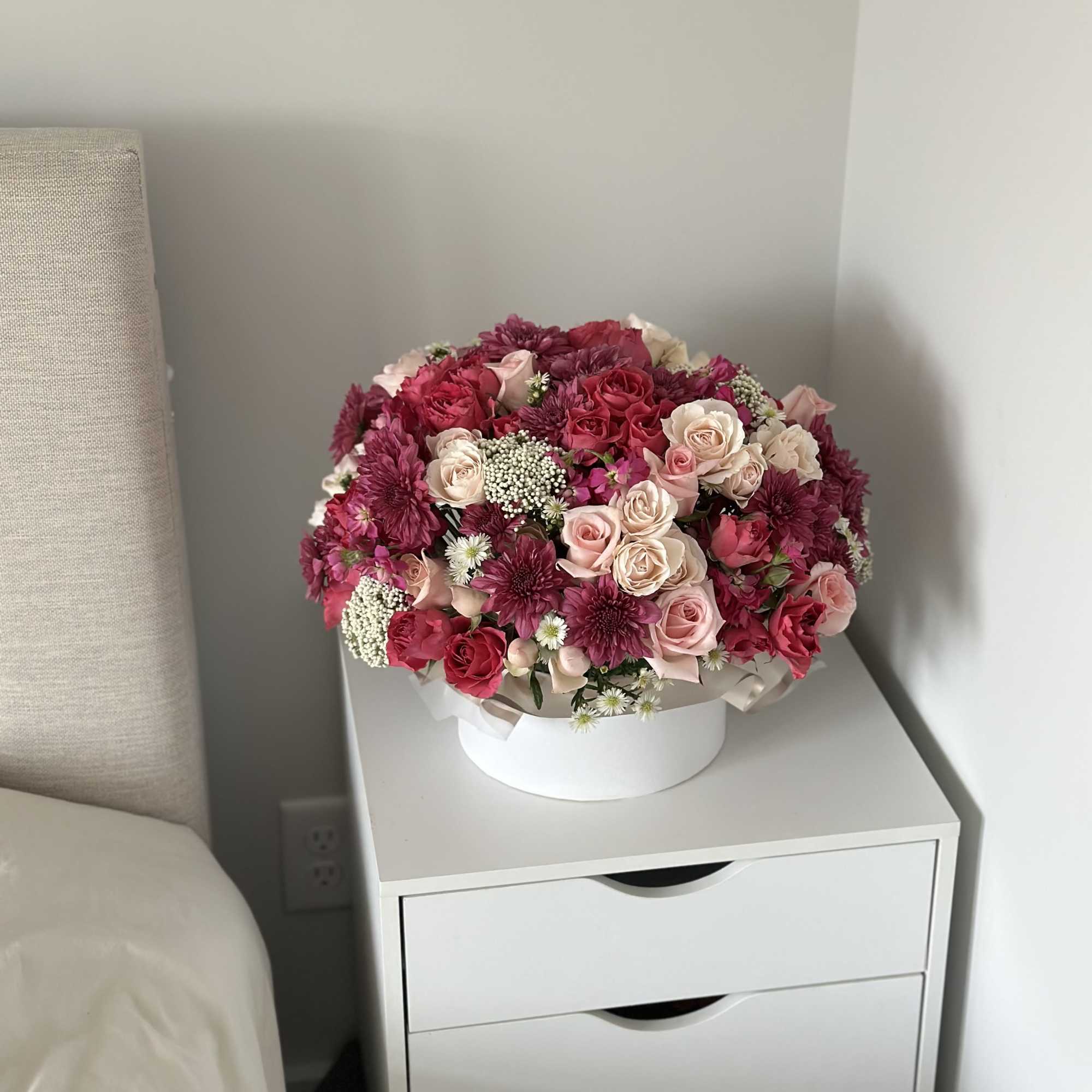 Round bouquet of pink and burgundy roses with small white filler flowers in a white box