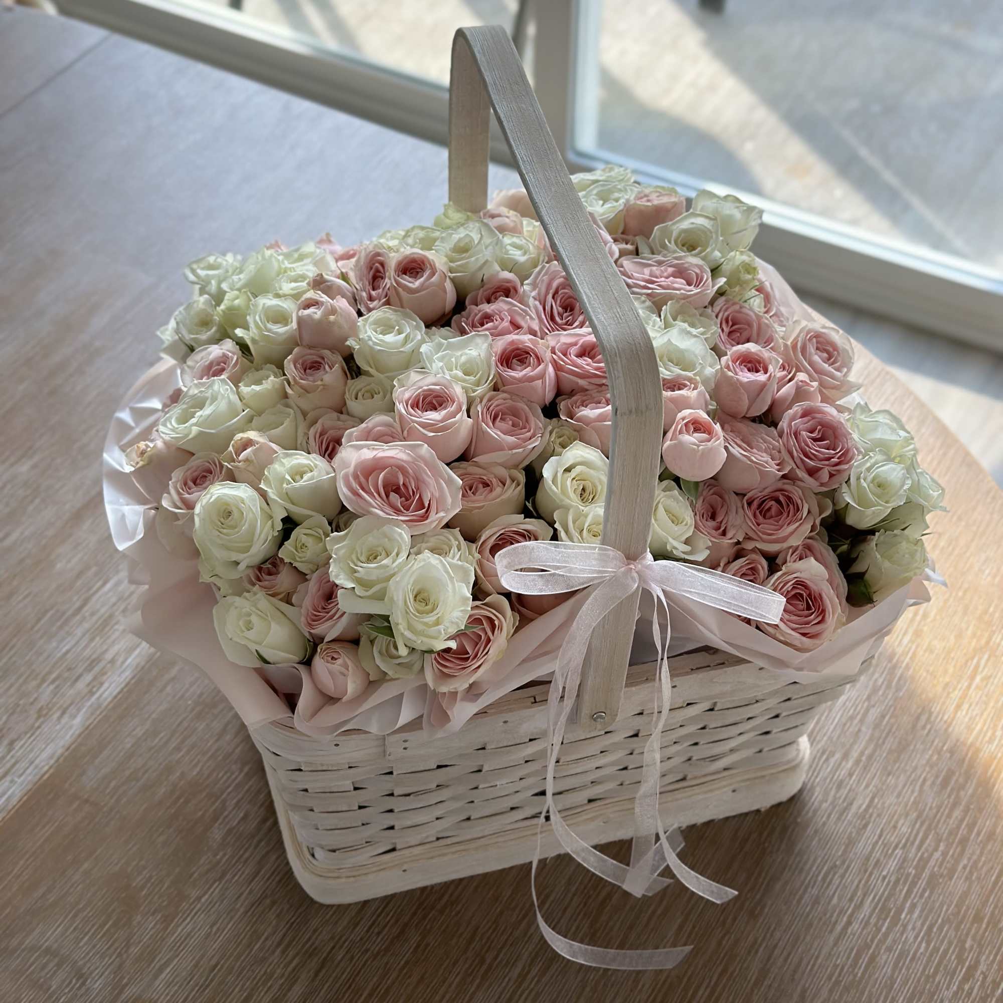 Basket of pink and white roses with a ribbon handle
