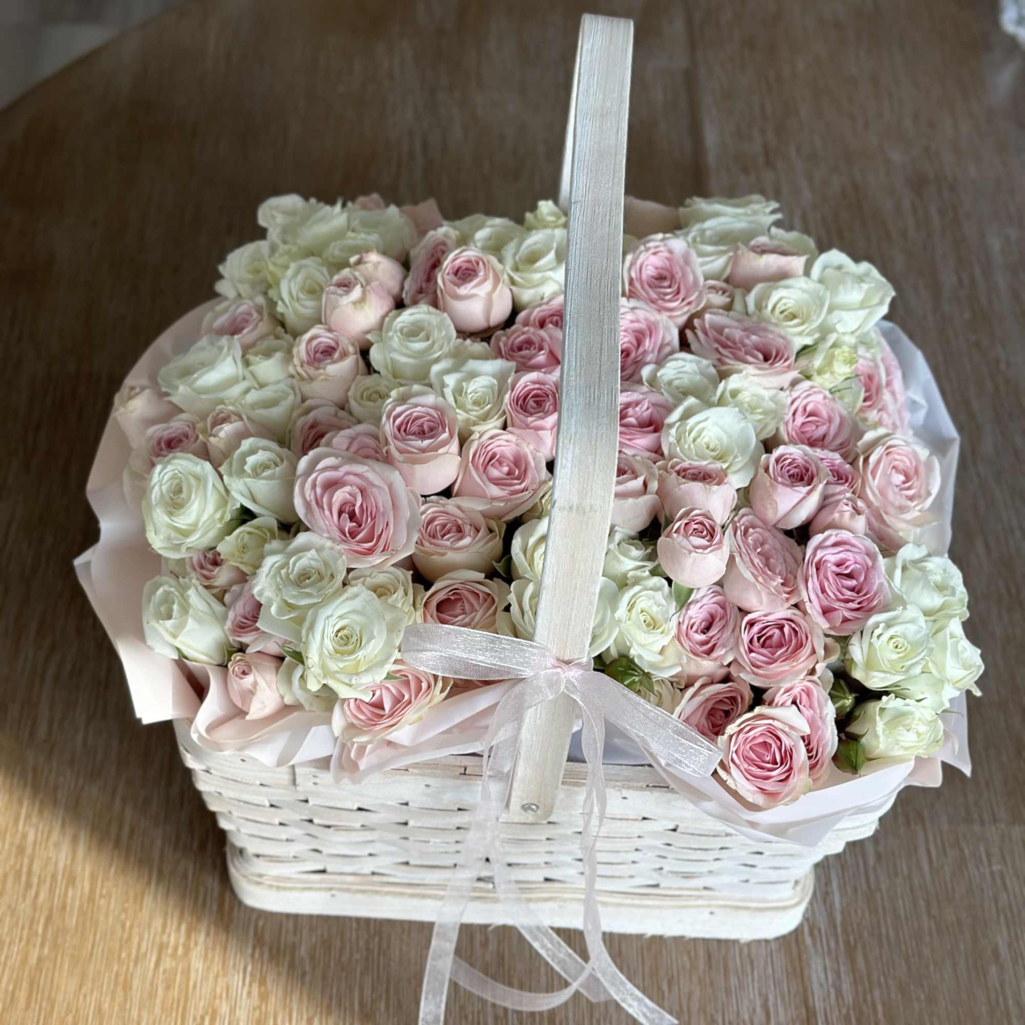 Basket of pink and white roses with a ribbon handle