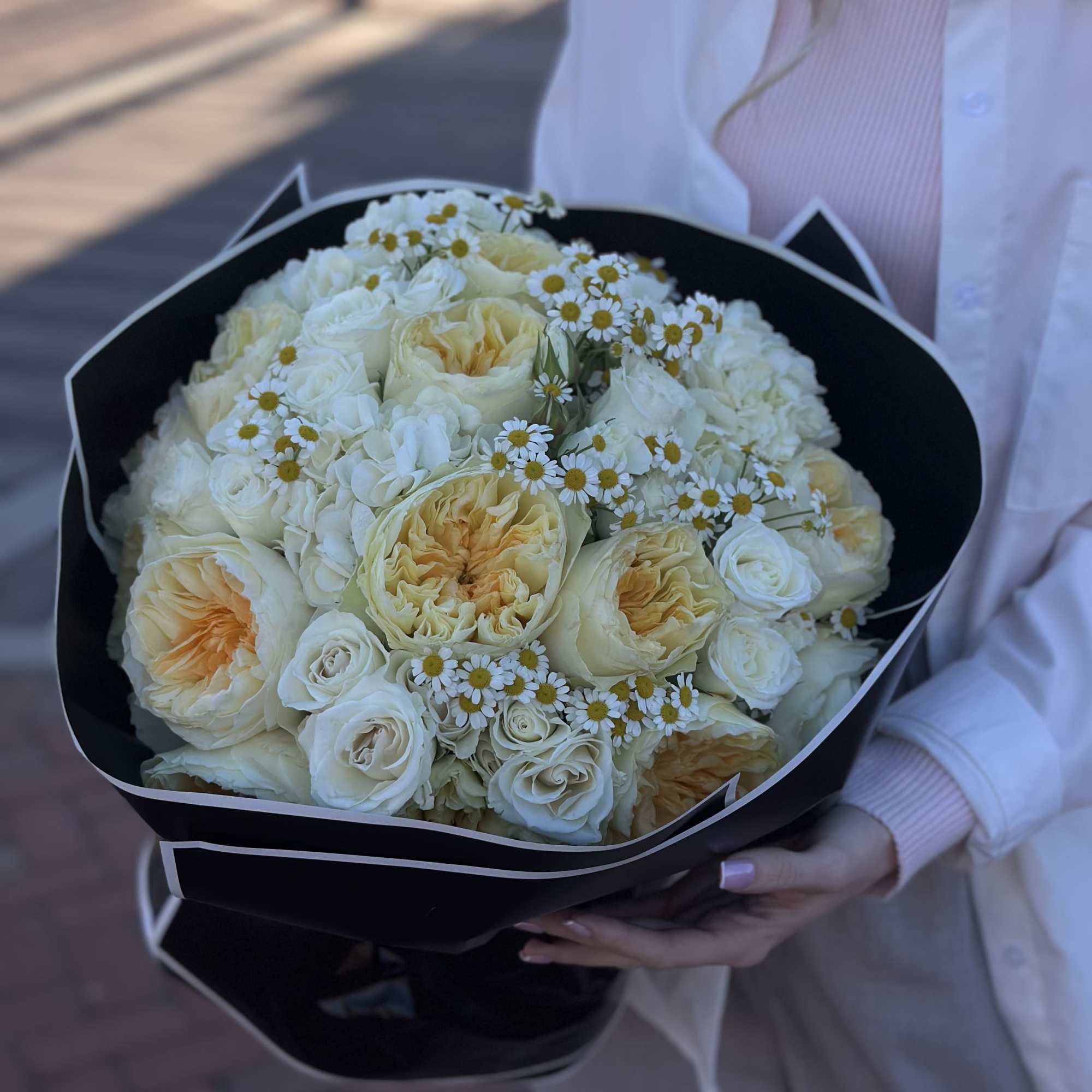 Bouquet of cream roses and small white daisies wrapped in black paper