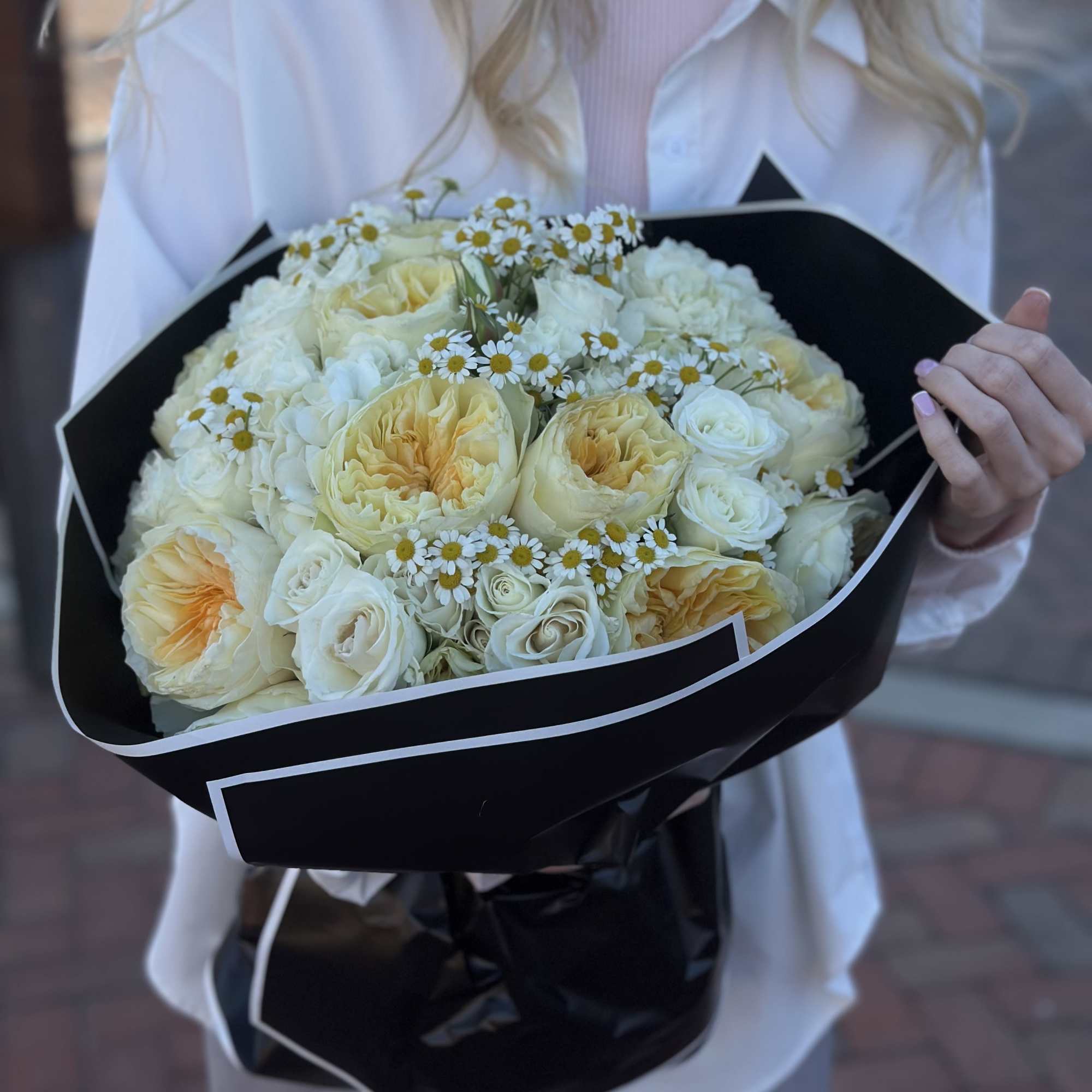 Bouquet of cream roses and small white daisies wrapped in black paper