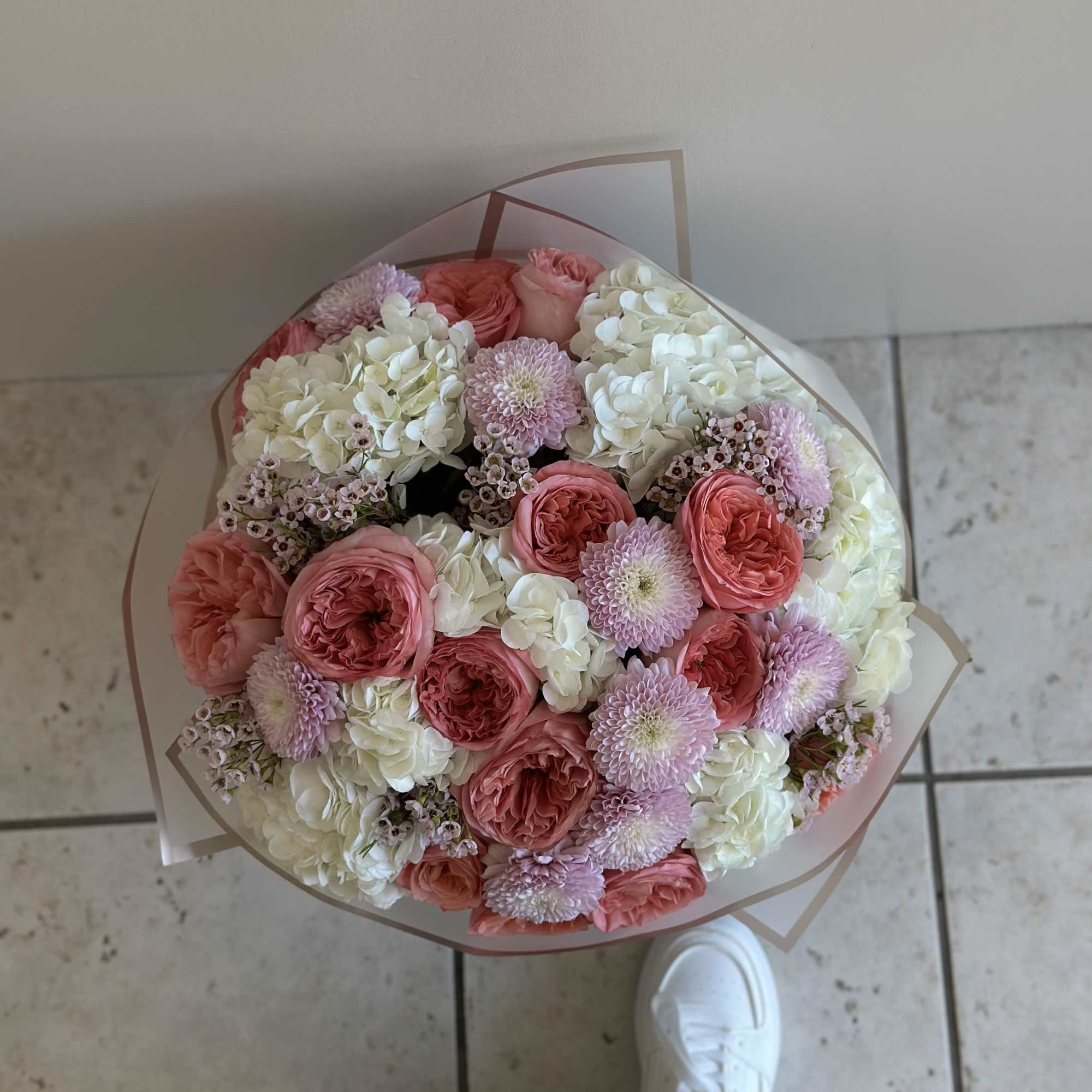 Round bouquet of pink and white flowers wrapped in clear paper