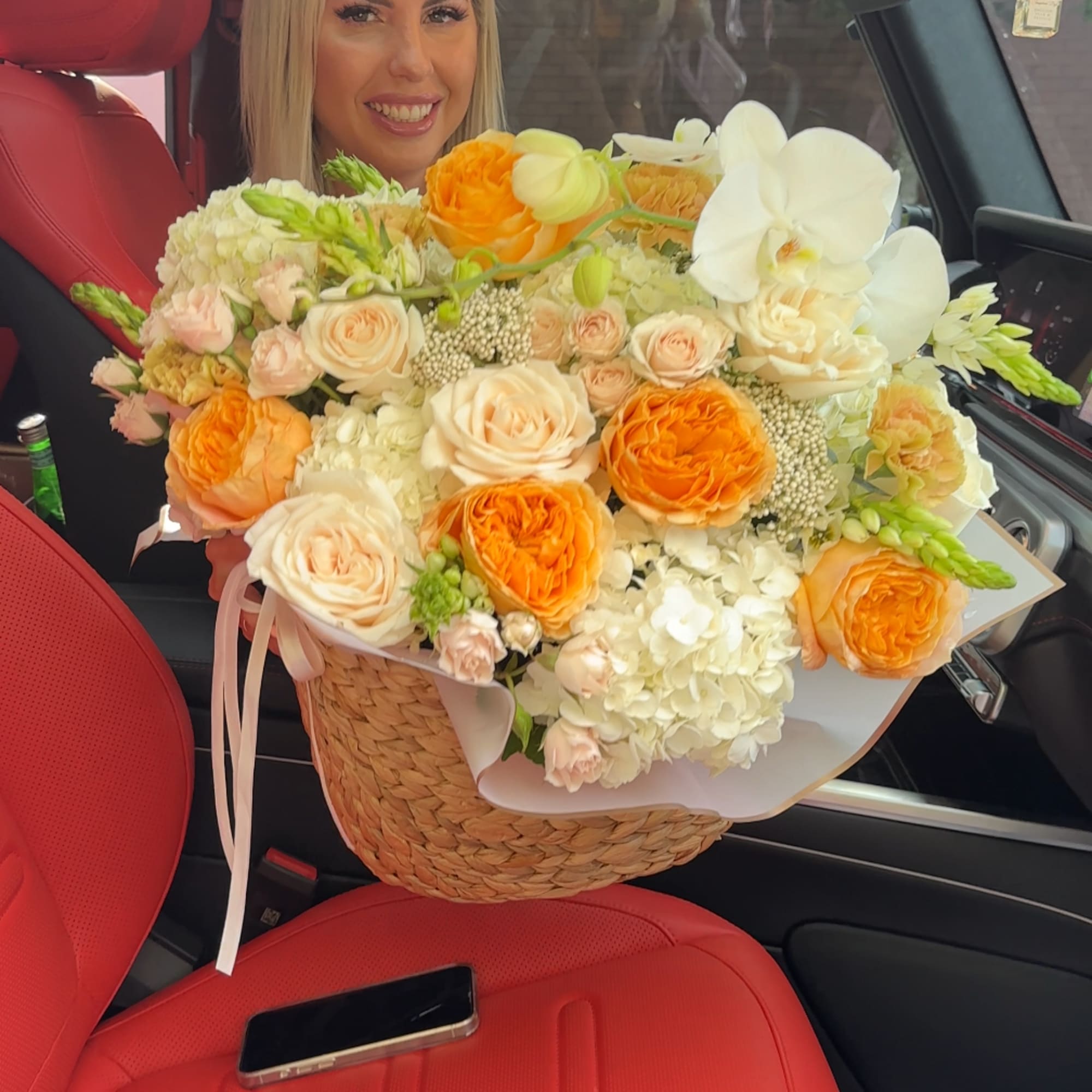 Woman holding a large bouquet of orange and cream flowers in a basket
