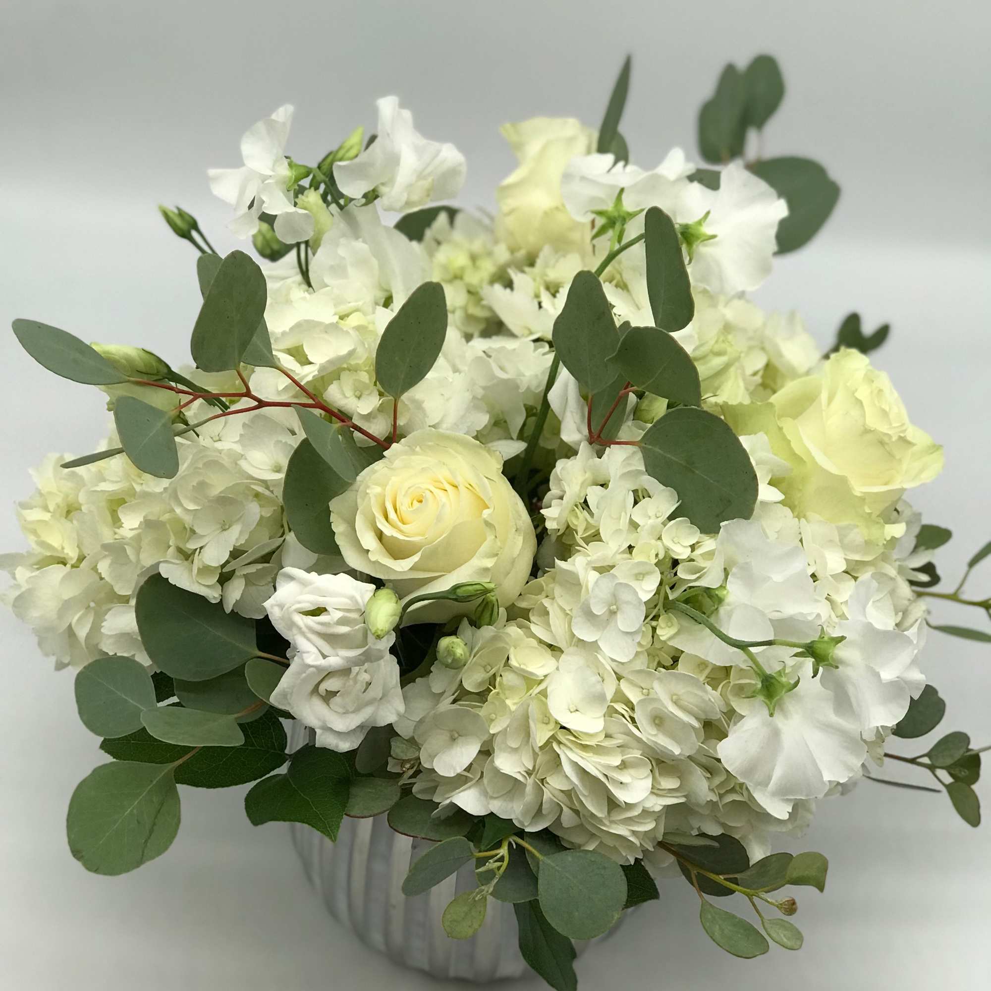 White and pale yellow flowers arranged in a clear vase with eucalyptus