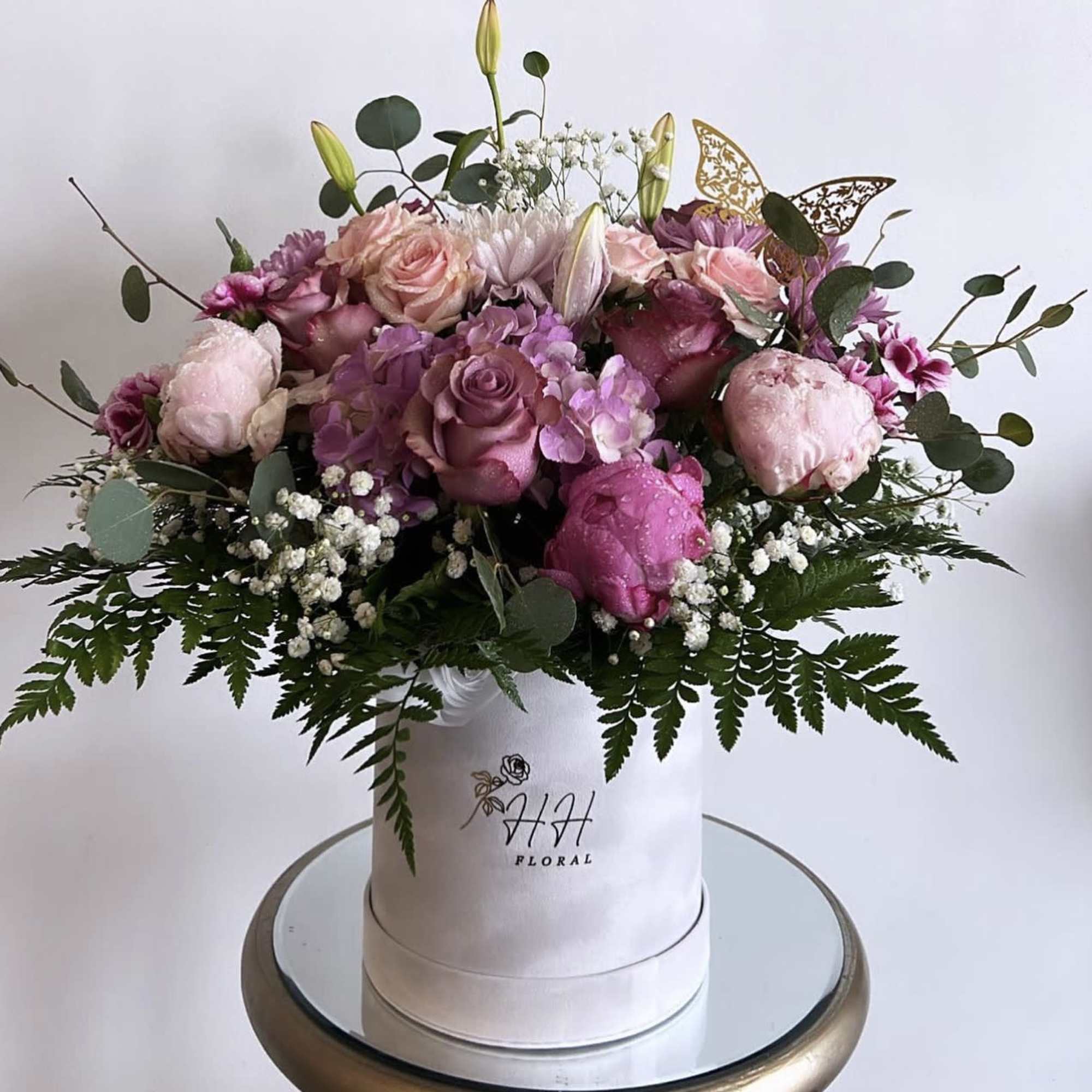 Pink and lavender roses arranged in a white hat box with greenery.