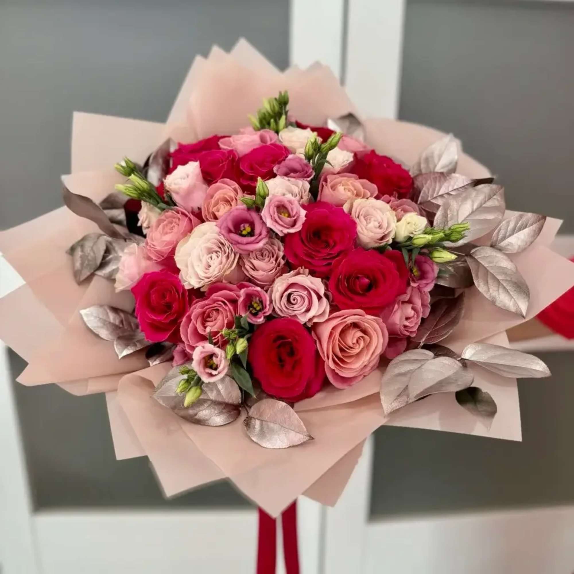Bouquet of pink and red roses wrapped in pale paper