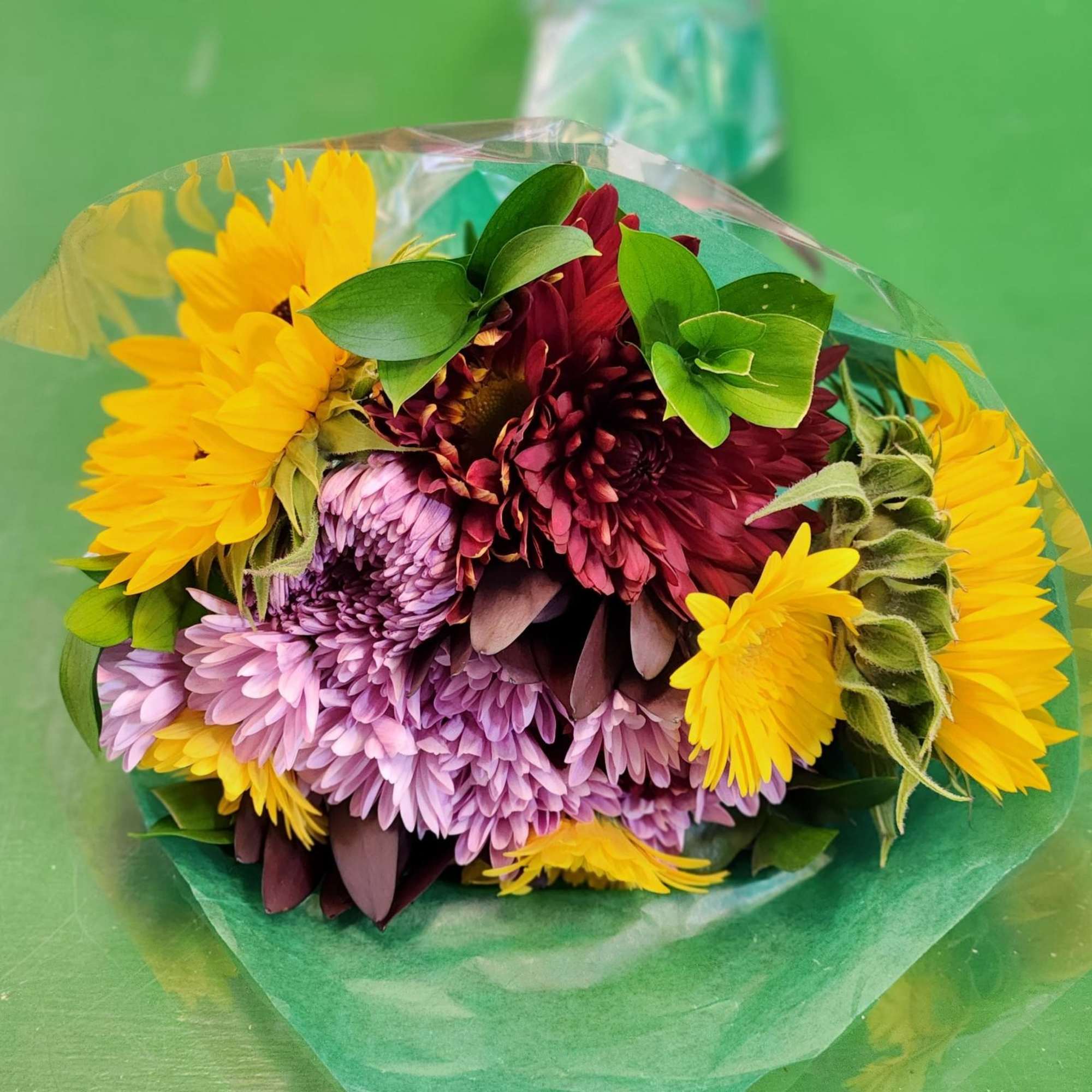 Bouquet of yellow, purple, and burgundy chrysanthemums wrapped in green paper