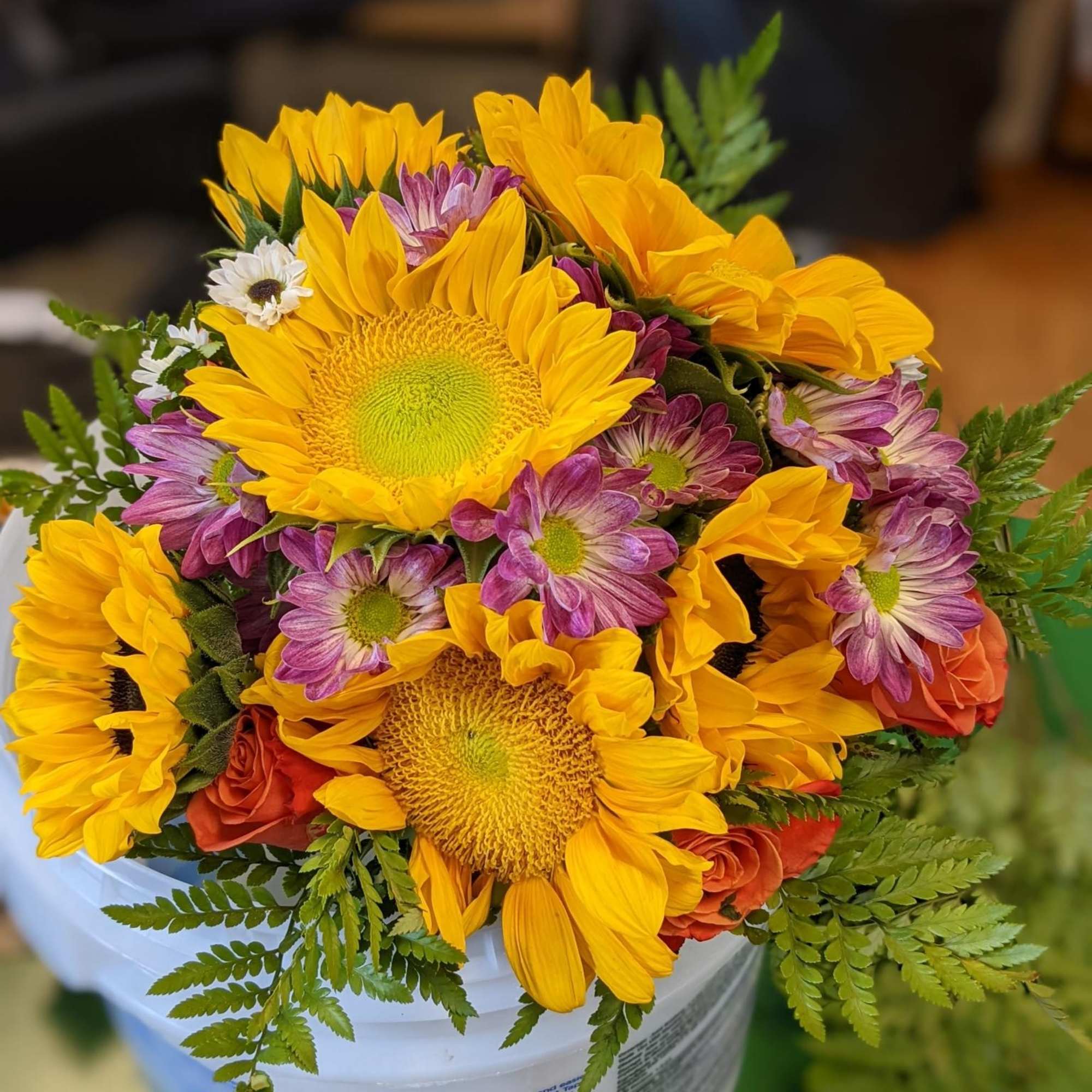 Bouquet of yellow sunflowers and purple daisies in a white bucket