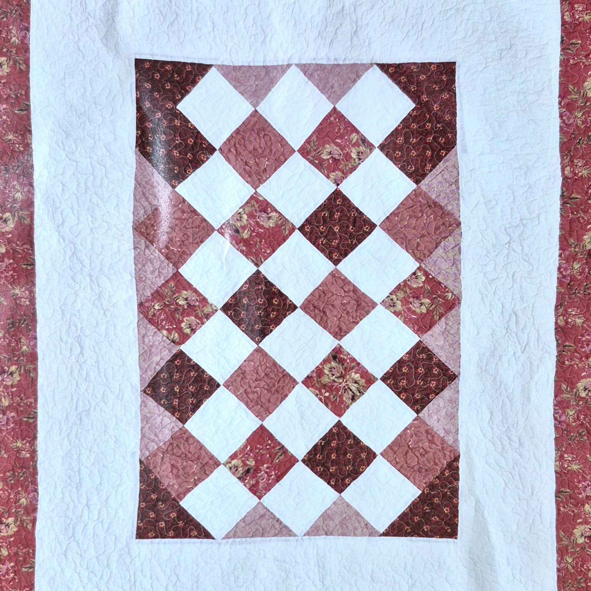 Patchwork quilt with a diamond pattern in pink, red, and white