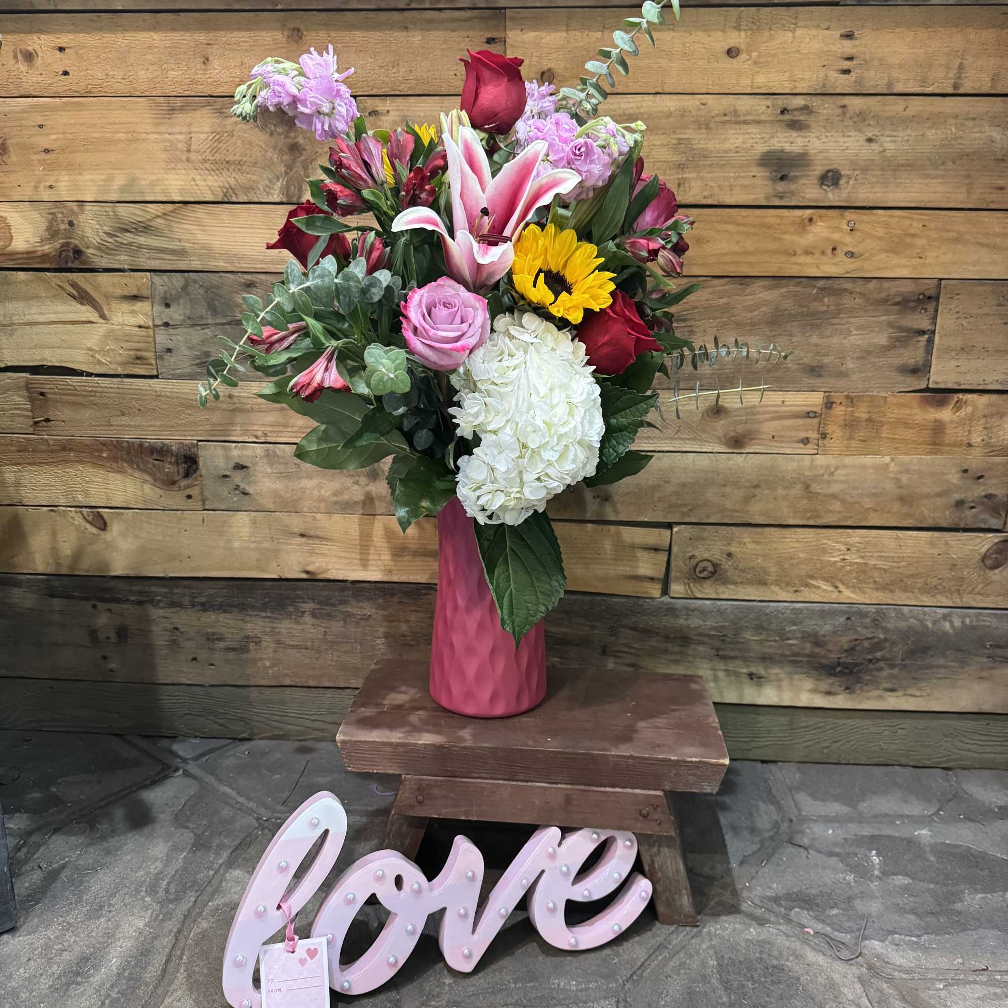 Pink and red mixed bouquet in a pink vase with a "love" sign below