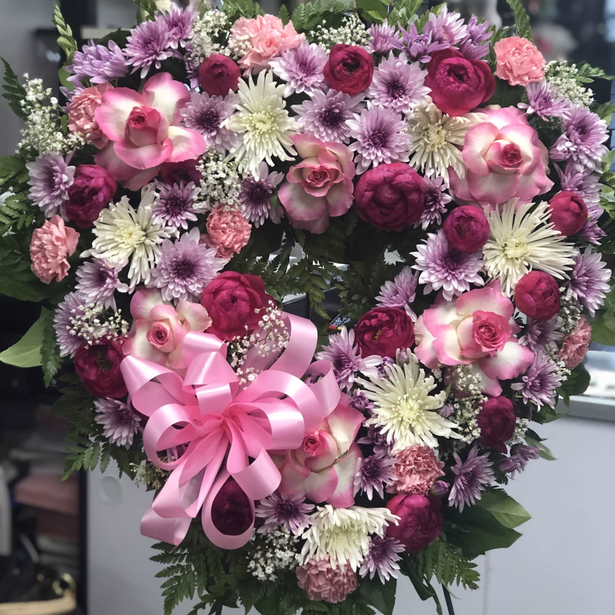 Heart-shaped floral wreath with pink and purple blooms and a pink ribbon bow
