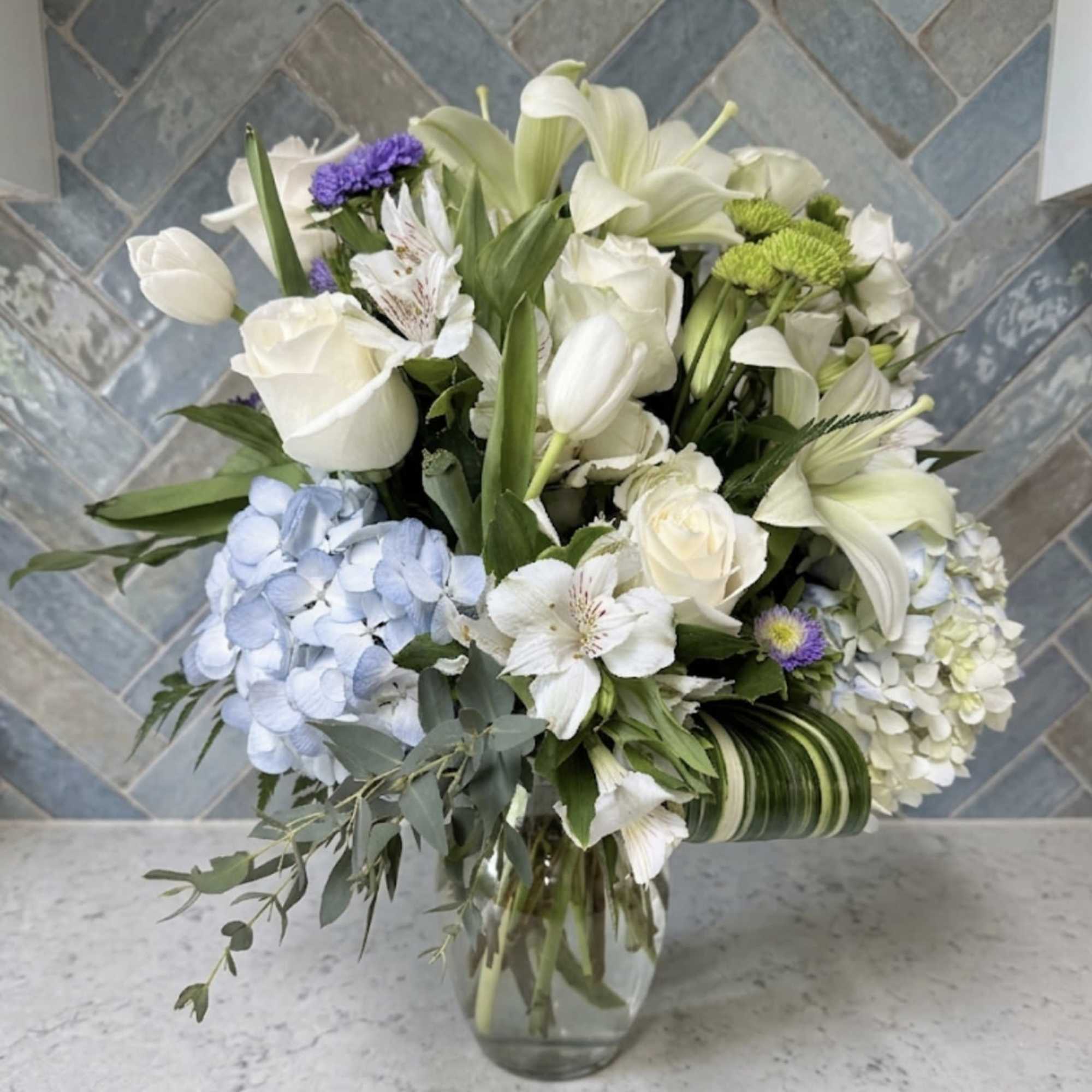 Soft white lilies and roses take center stage in this sympathy flower