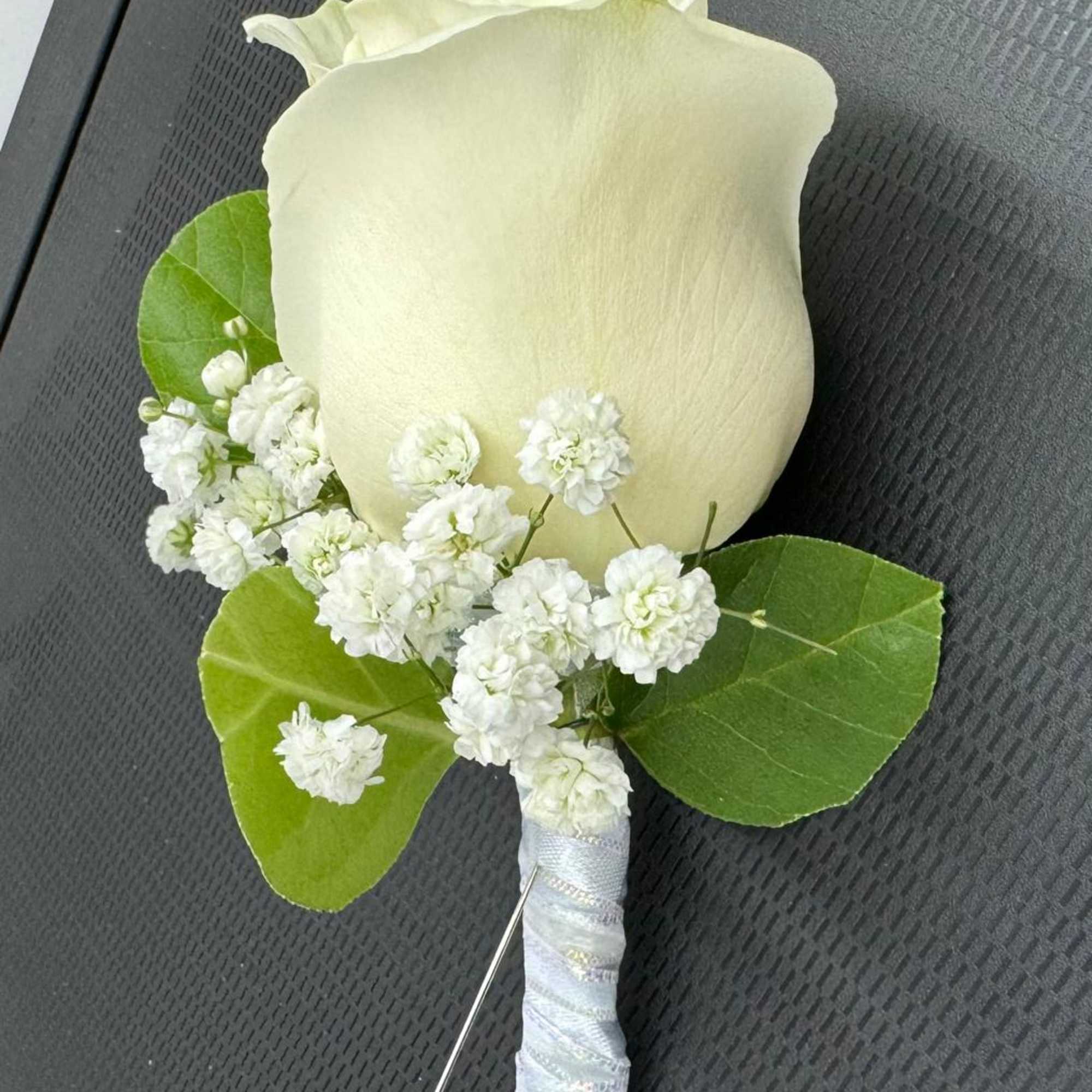 White rose boutonniere with baby's breath and green leaves