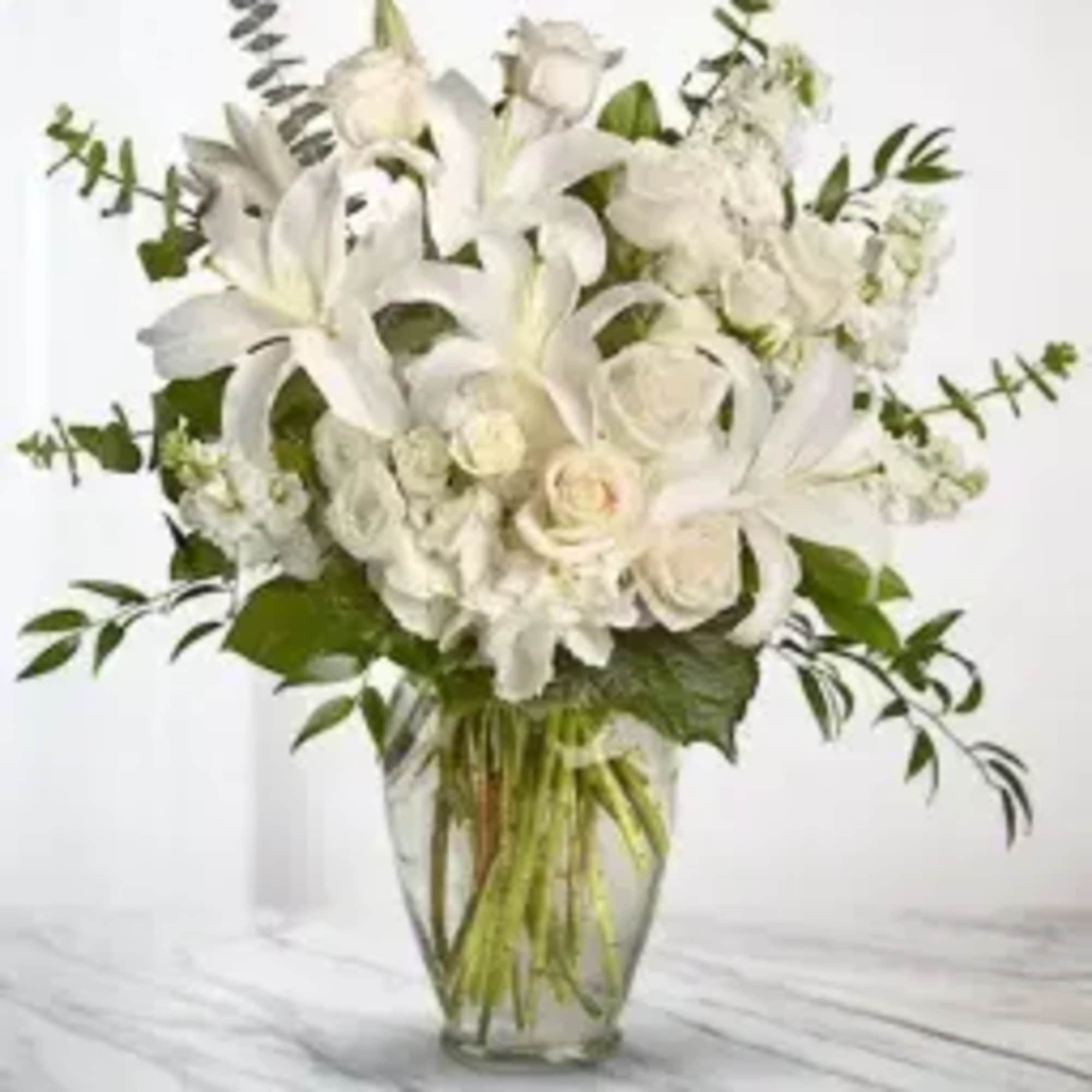 White lilies and roses arranged in a clear glass vase