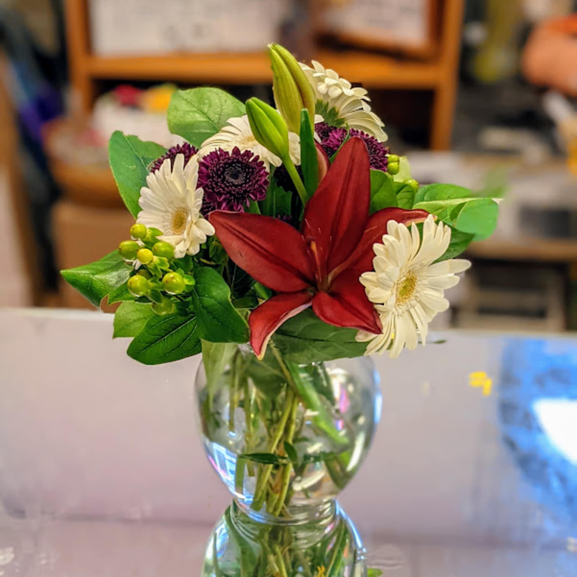 Mixed bouquet with red lily, white daisies, and purple blooms in a glass vase