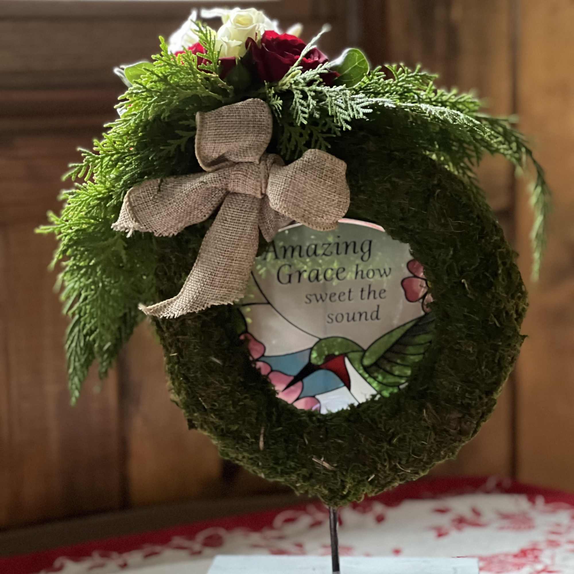 Moss wreath with red and white roses and a burlap bow on a stand