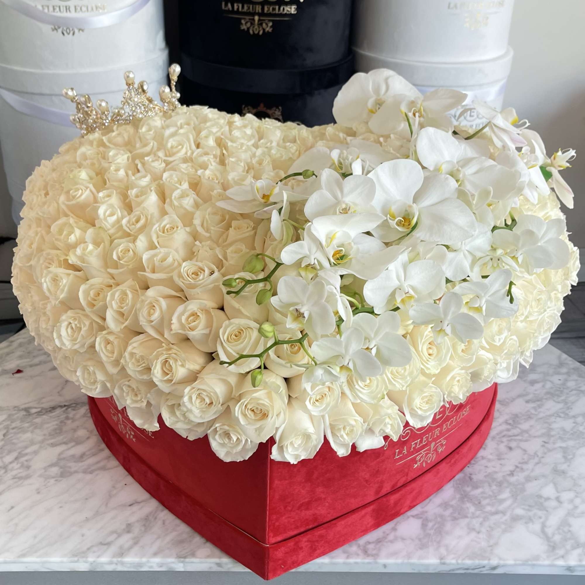 Cream rose arrangement with white orchids in a red heart-shaped box