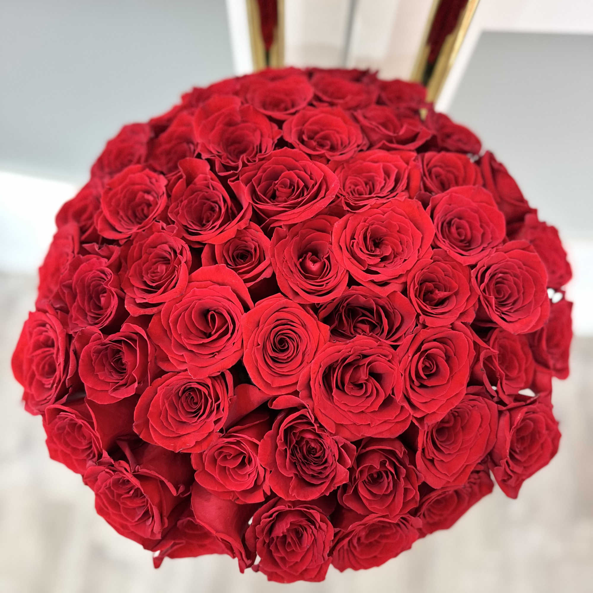 Round bouquet of red roses with gold ribbon handles