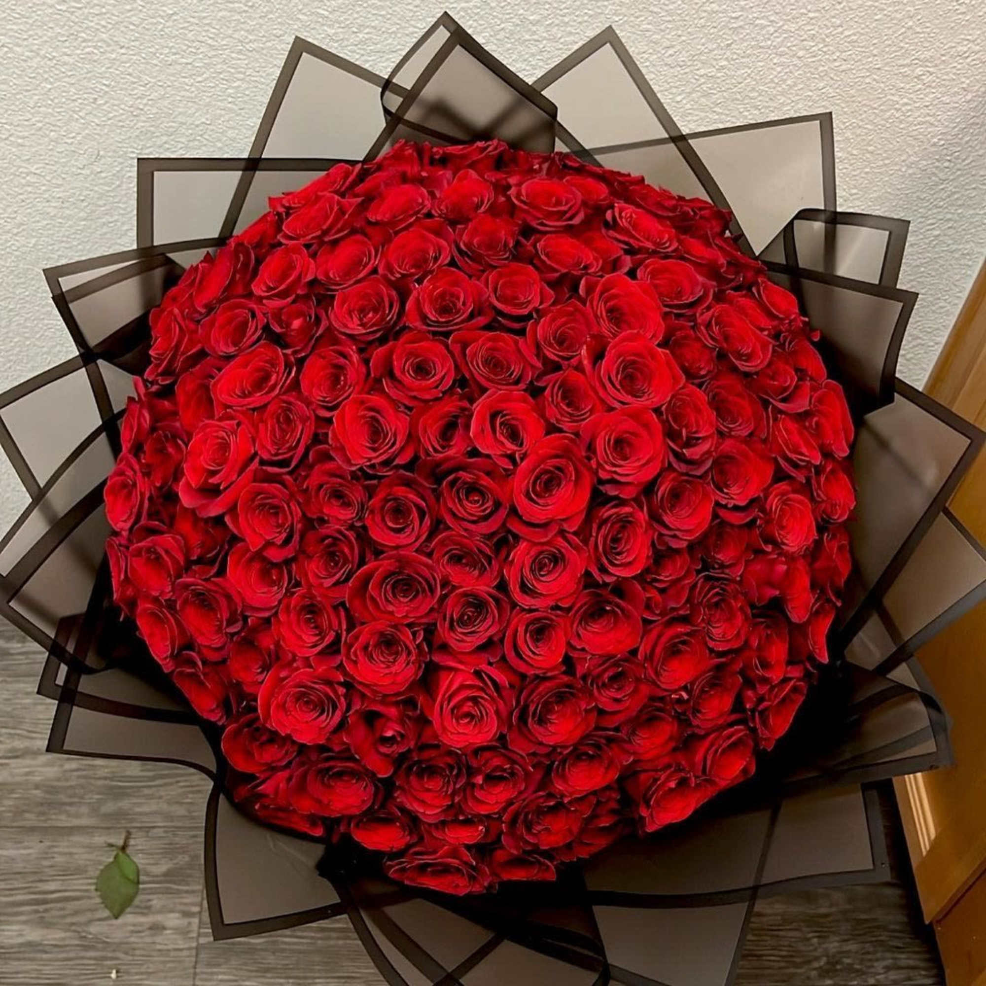 Large round bouquet of tightly packed red roses wrapped in dark translucent paper