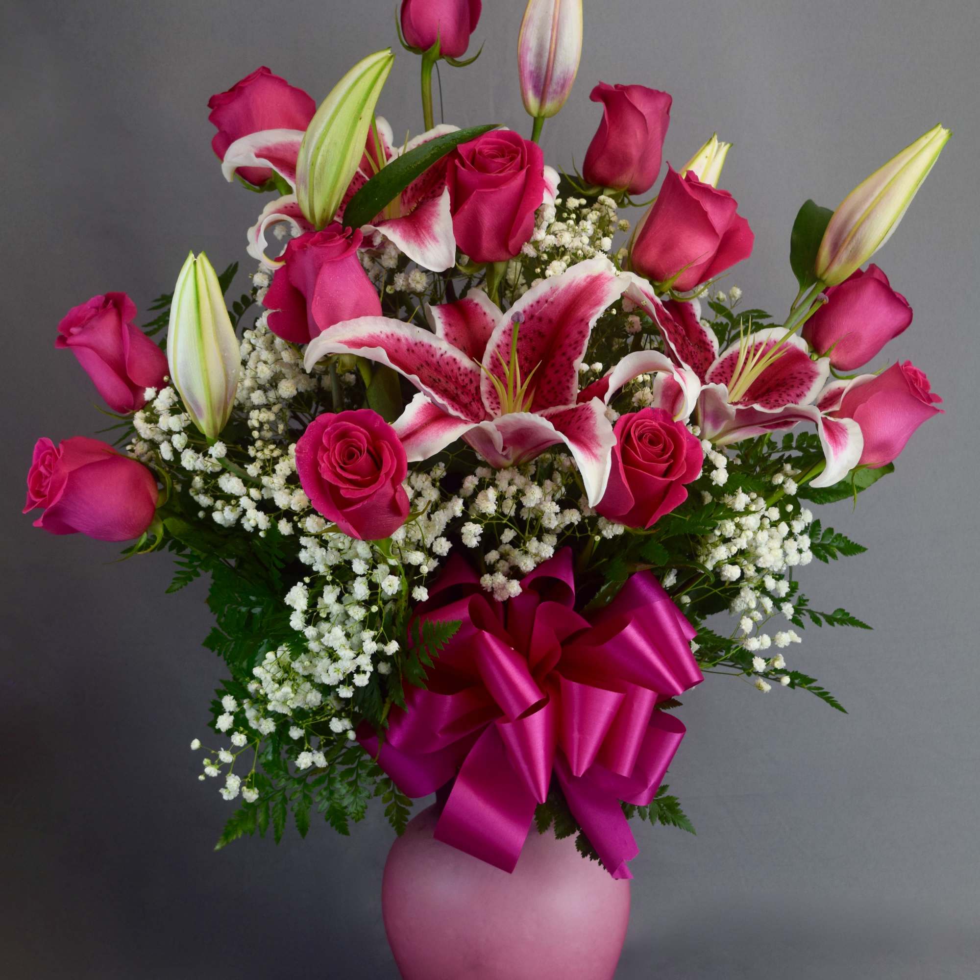 Pink roses and lilies in a pink vase with a large ribbon